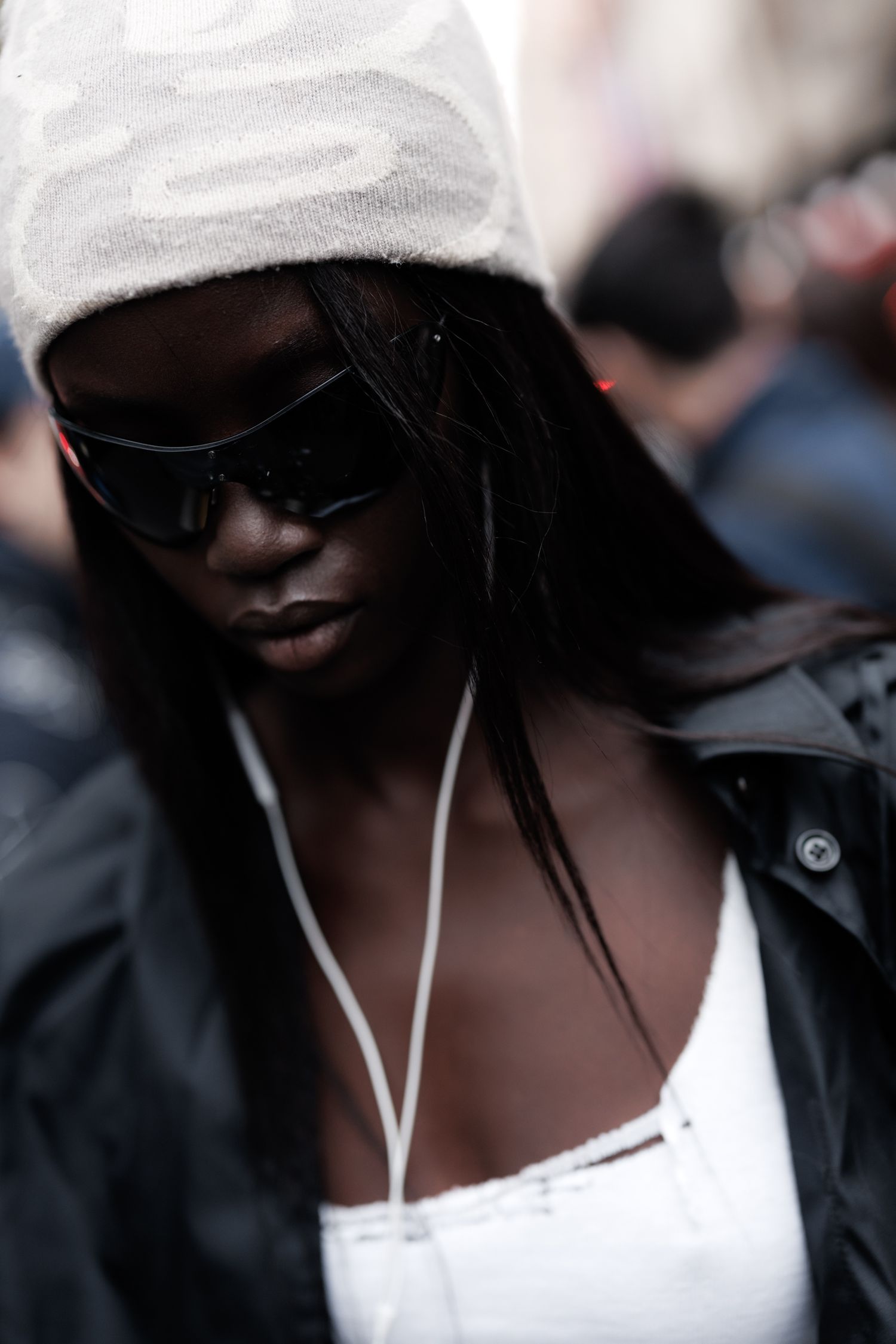Individual in a black hoodie and white top walks through a crowded outdoor space.