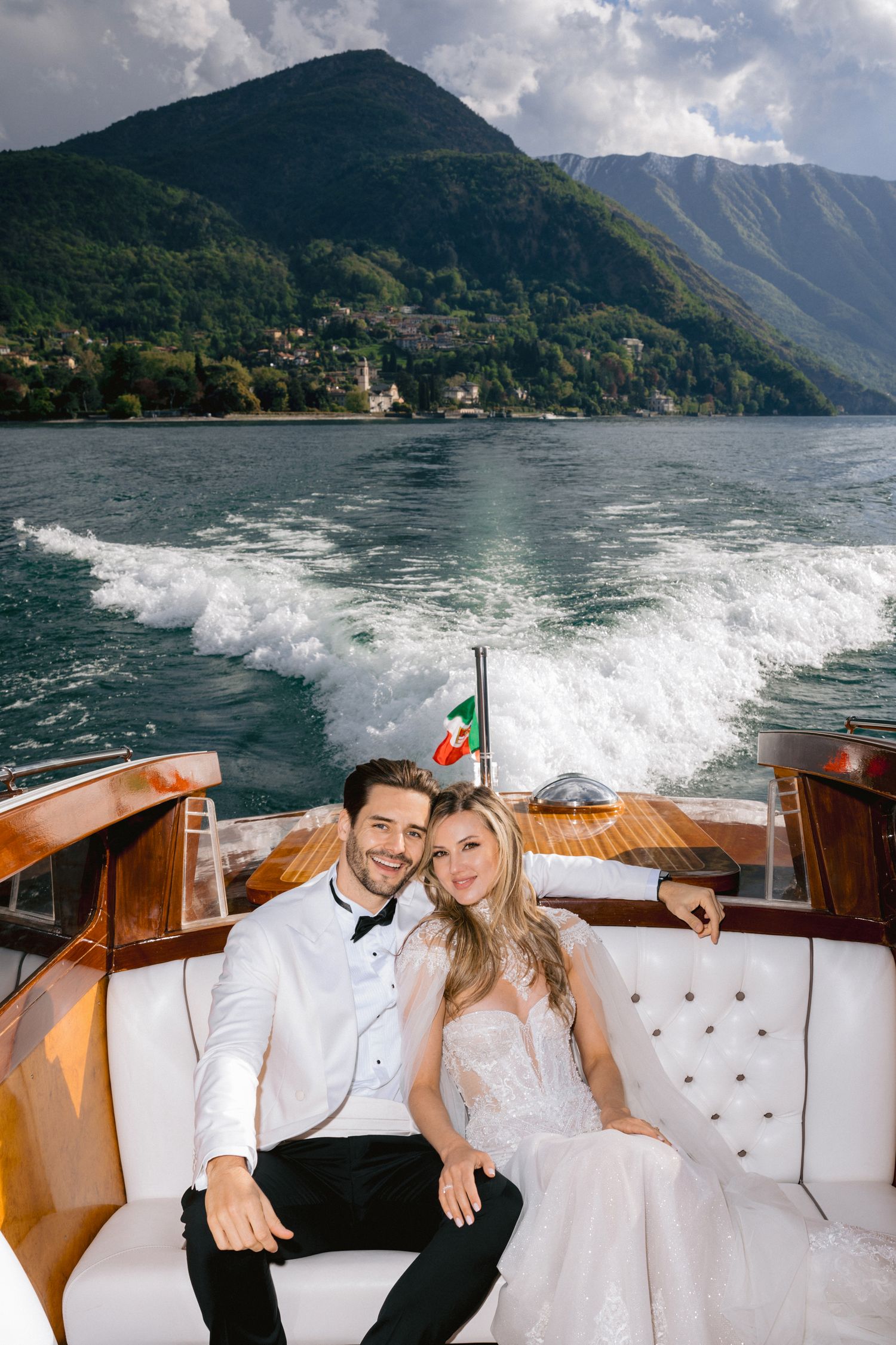 Couple enjoying boat ride on Lake Como with mountains and wake in background.