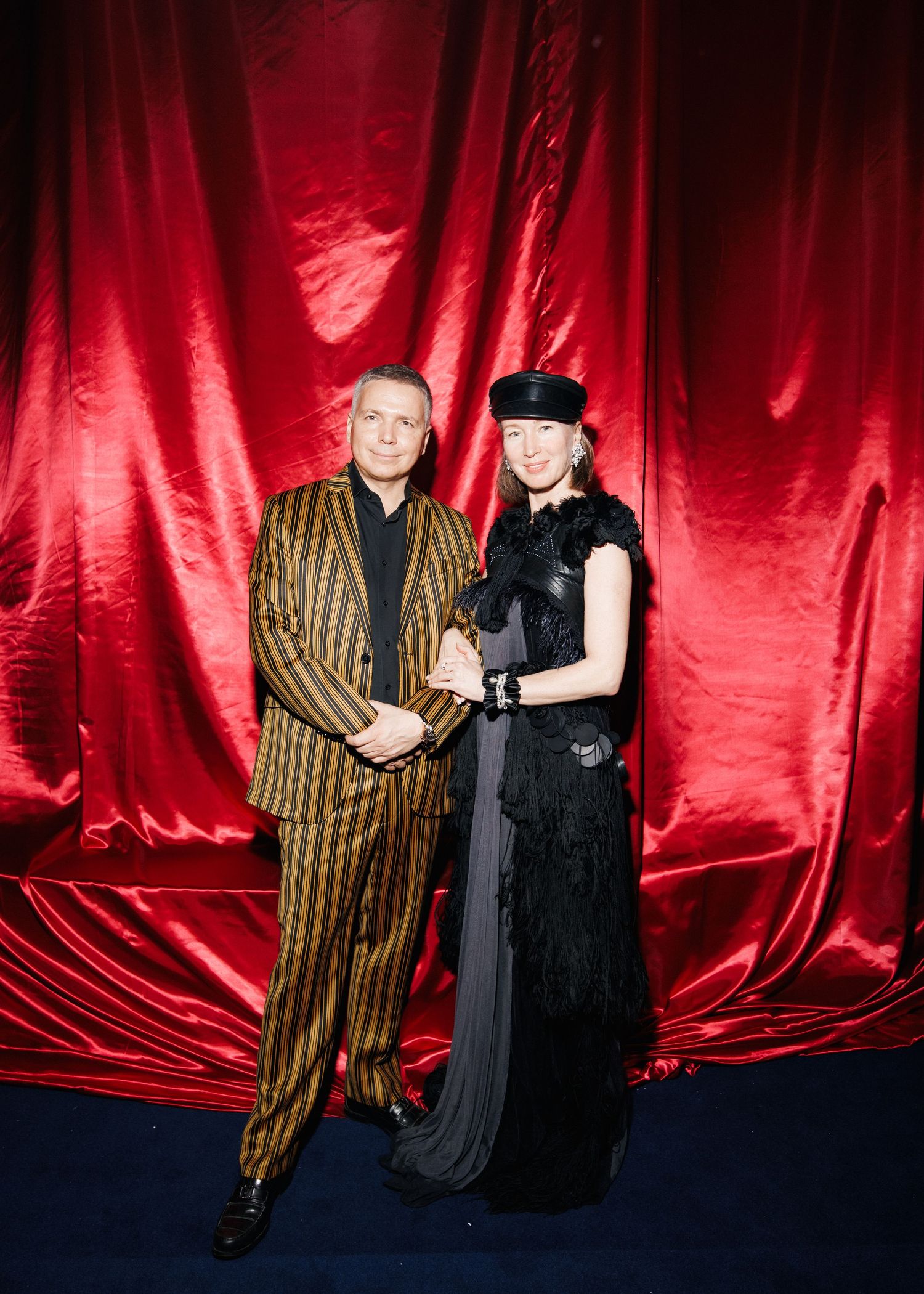 Couple posing against red velvet backdrop in contrasting formal attire.