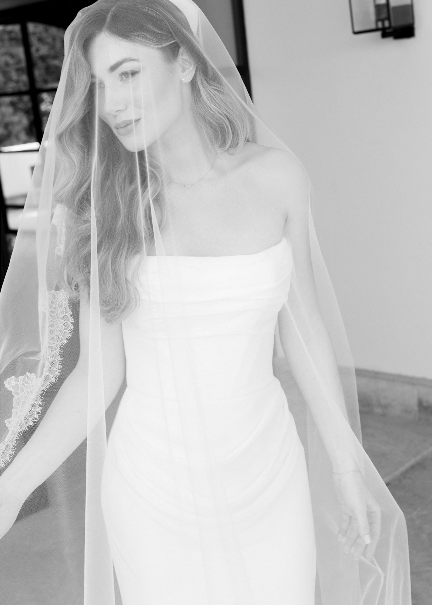 Bride wearing a strapless white wedding gown and lace-trimmed veil in a black and white portrait photo.
