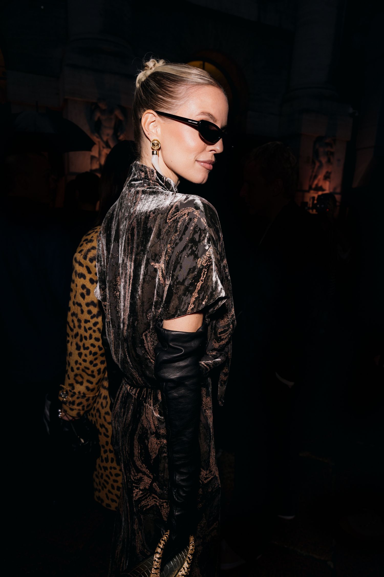 Fashion model wearing black sheer jacket and leopard print accessory poses against dark background.