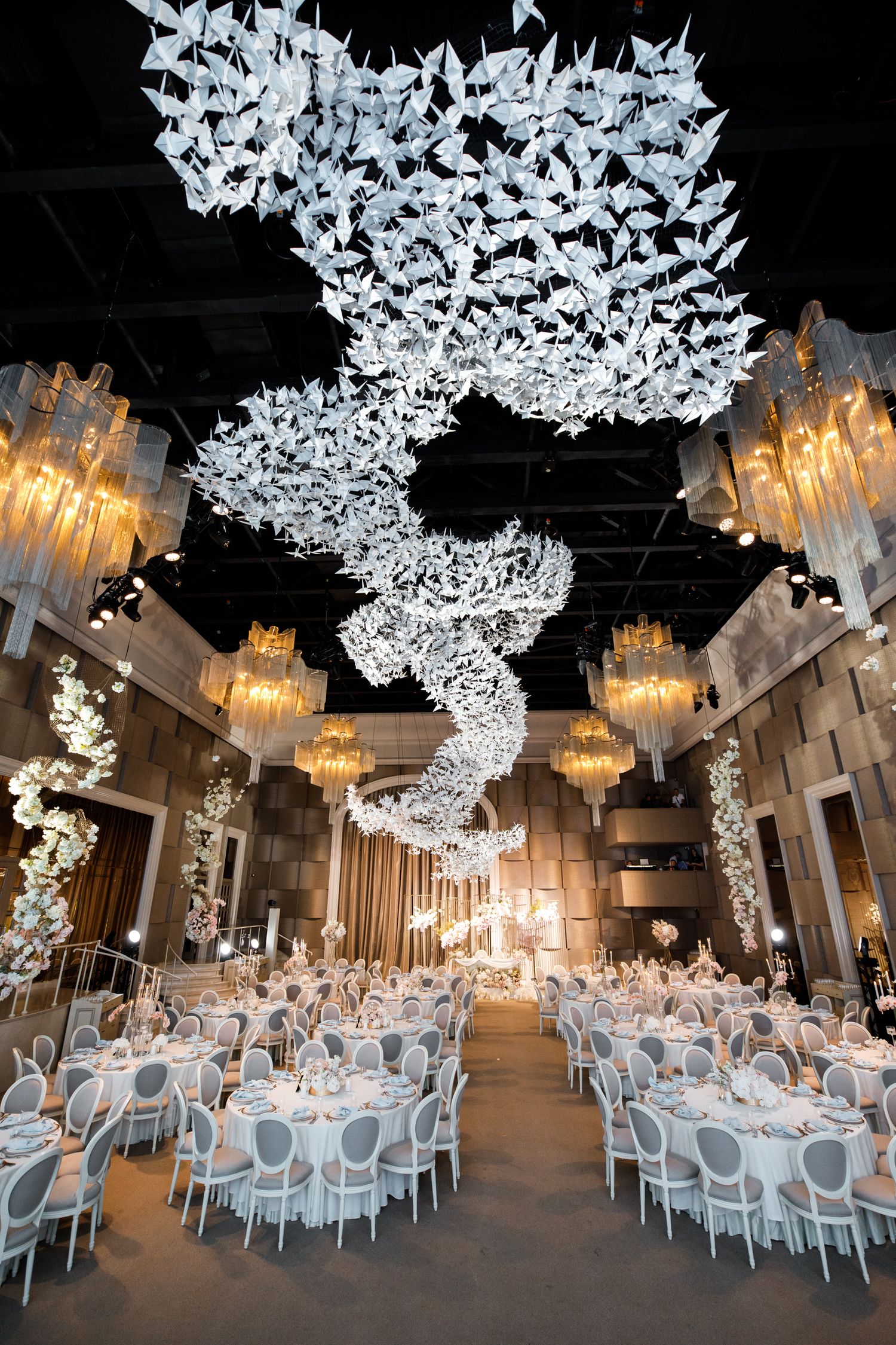 Elegant wedding reception venue with dramatic spiral butterfly ceiling installation and gold chandeliers.