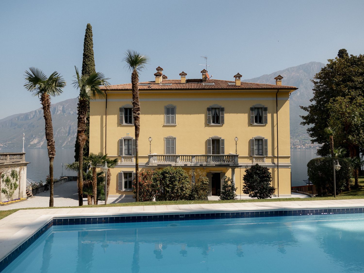 Mediterranean villa with yellow stucco exterior and multiple swimming pools surrounded by palm trees and landscaping.