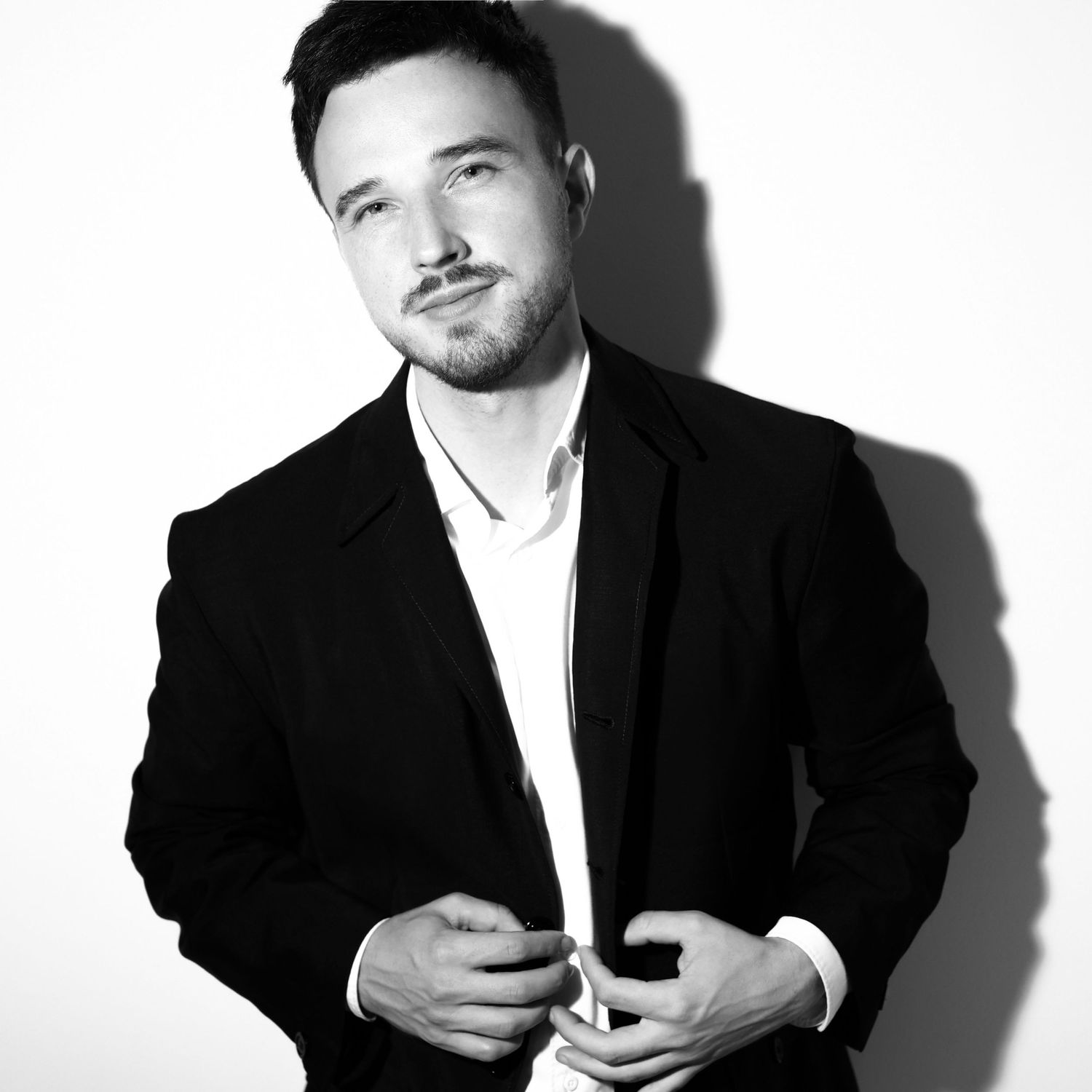 Dramatic black and white portrait of person in suit jacket against white background.