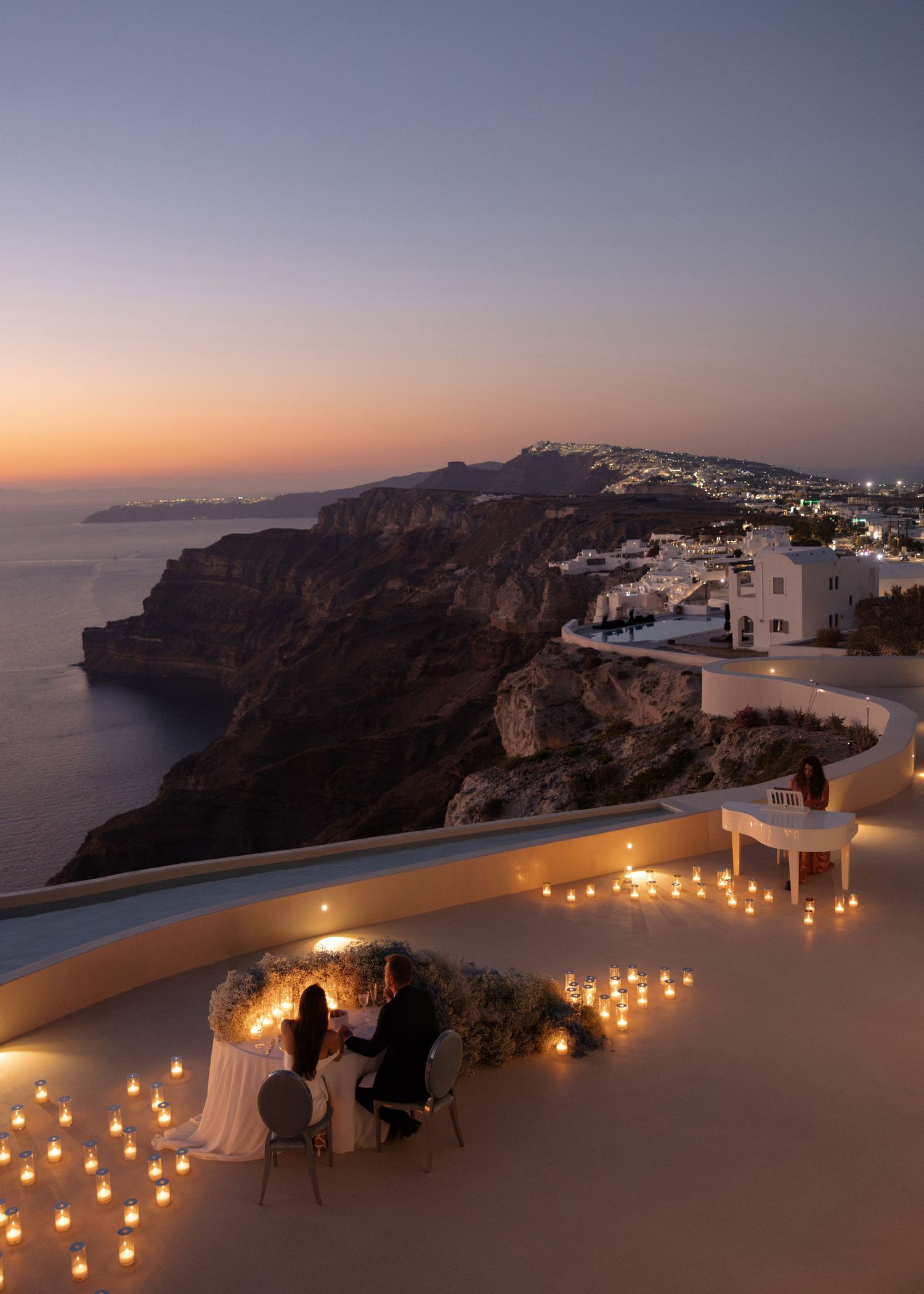 Romantic candlelit dinner for two on a Santorini cliffside terrace at sunset with stunning Aegean Sea views.