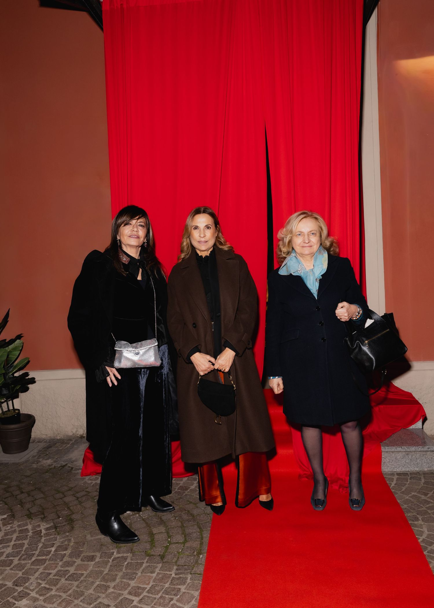 Three people pose together on a red carpet against a bright red curtain backdrop.