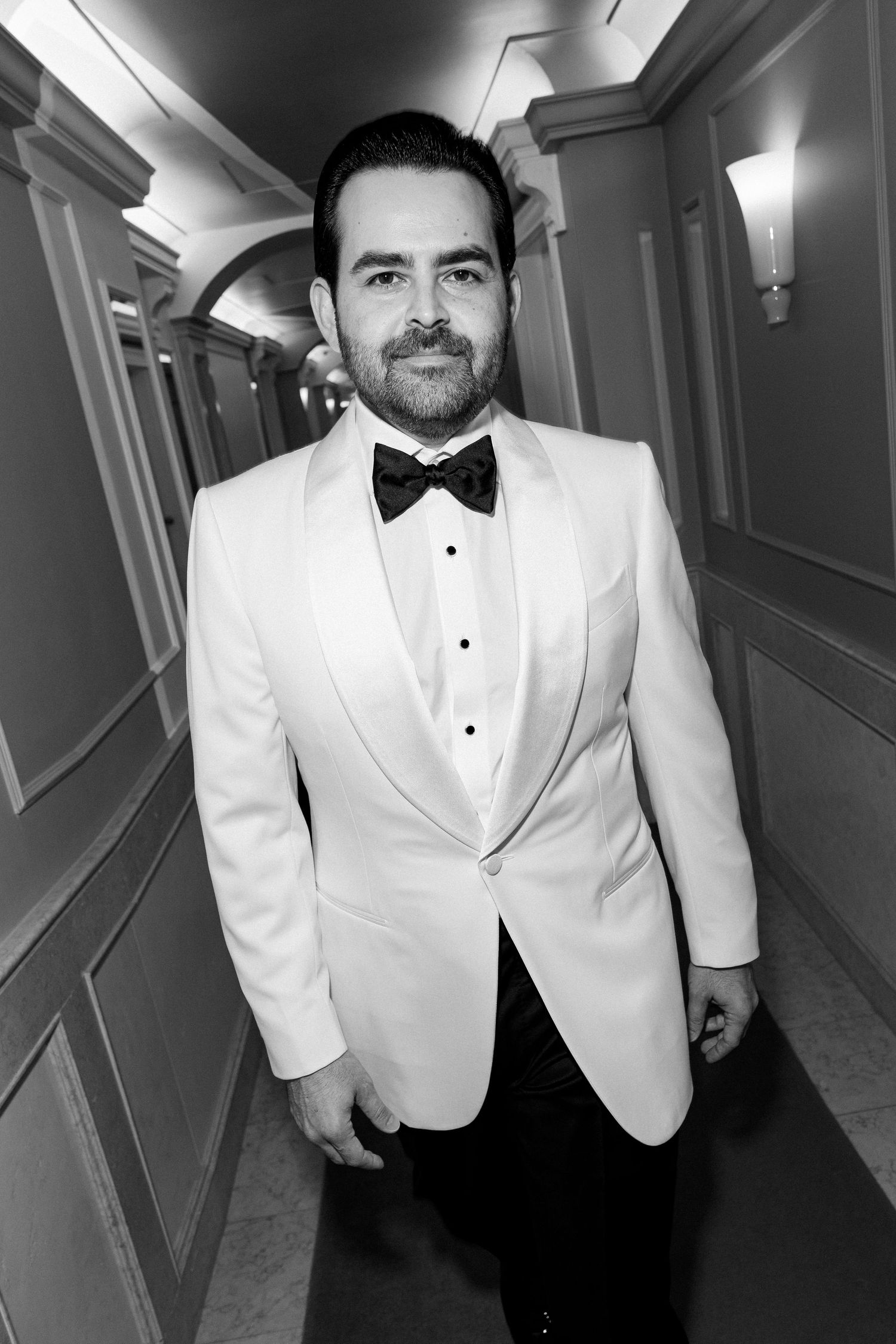 Person in white tuxedo jacket and bow tie photographed in hallway.