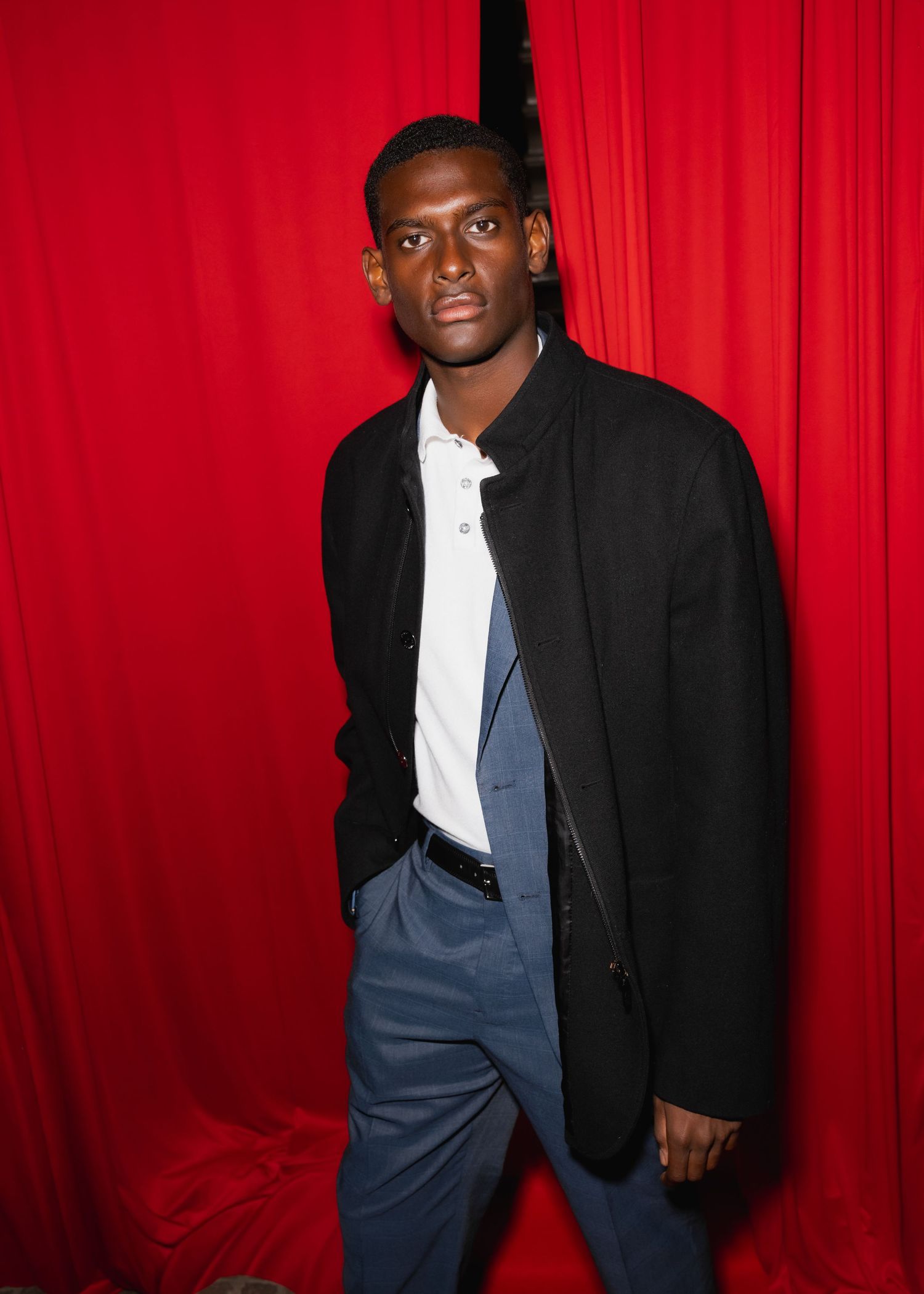 A person in a black jacket and white shirt poses in front of a red curtain background in a photo sequence.