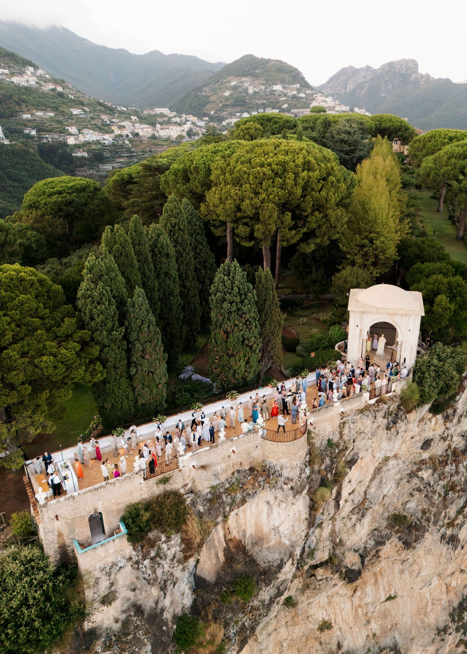 Aerial view of a wedding ceremony on a cliffside terrace in Ravello, Amalfi Coast, surrounded by lush greenery and mountains.