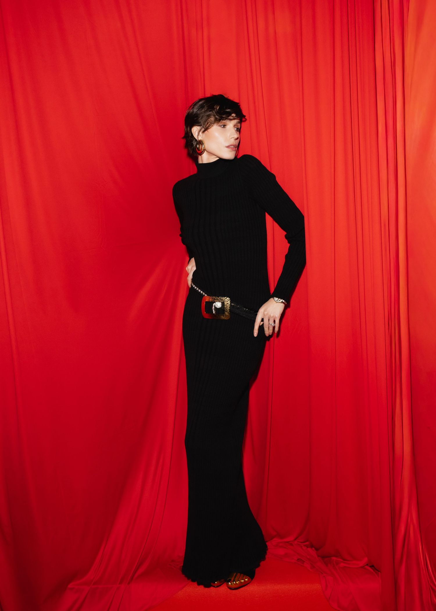 Figure in black dress poses against vibrant red curtain backdrop in artistic fashion photoshoot sequence.