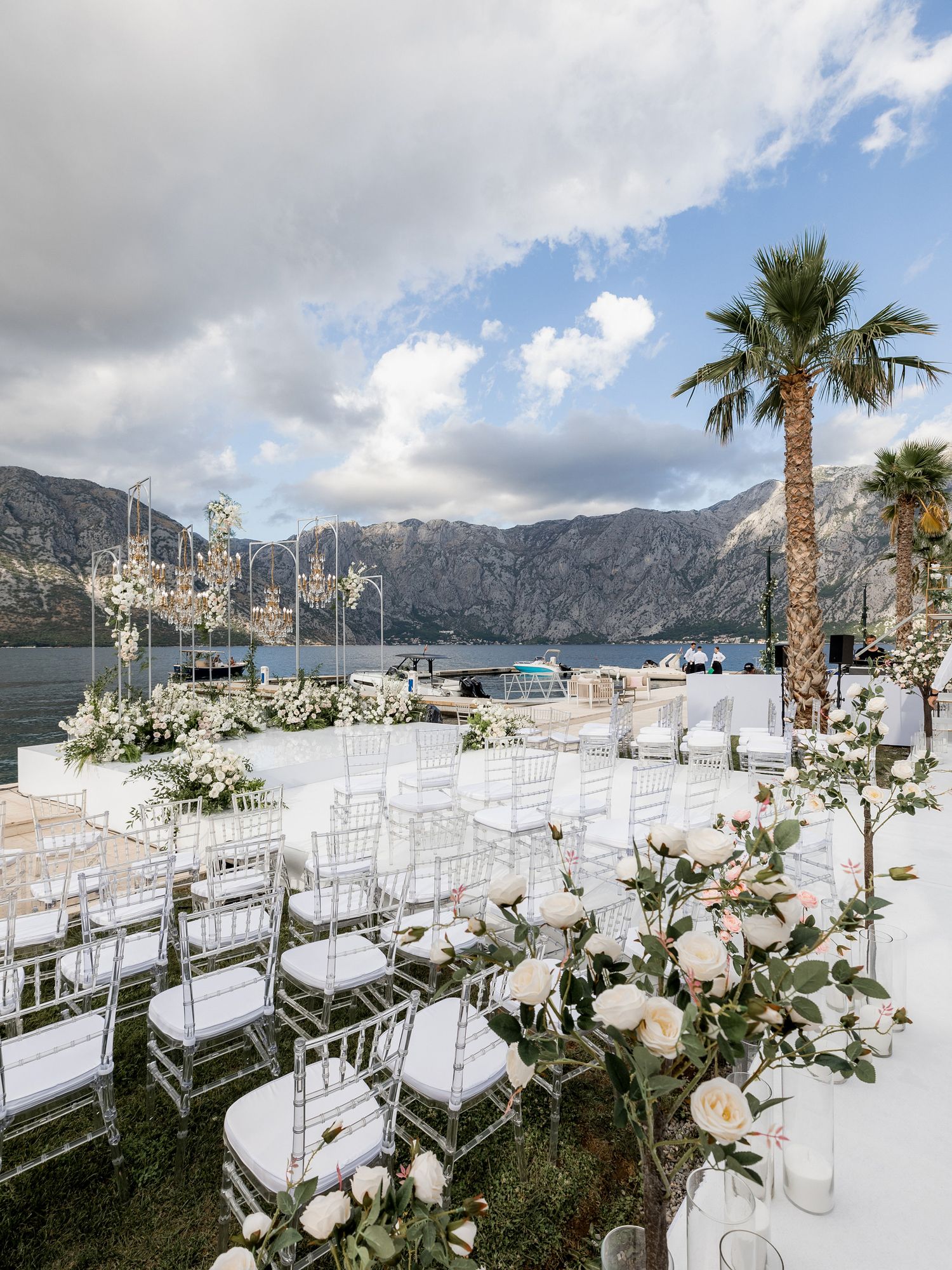 Elegant lakeside wedding ceremony setup with white chairs and floral decorations against a mountainous backdrop.