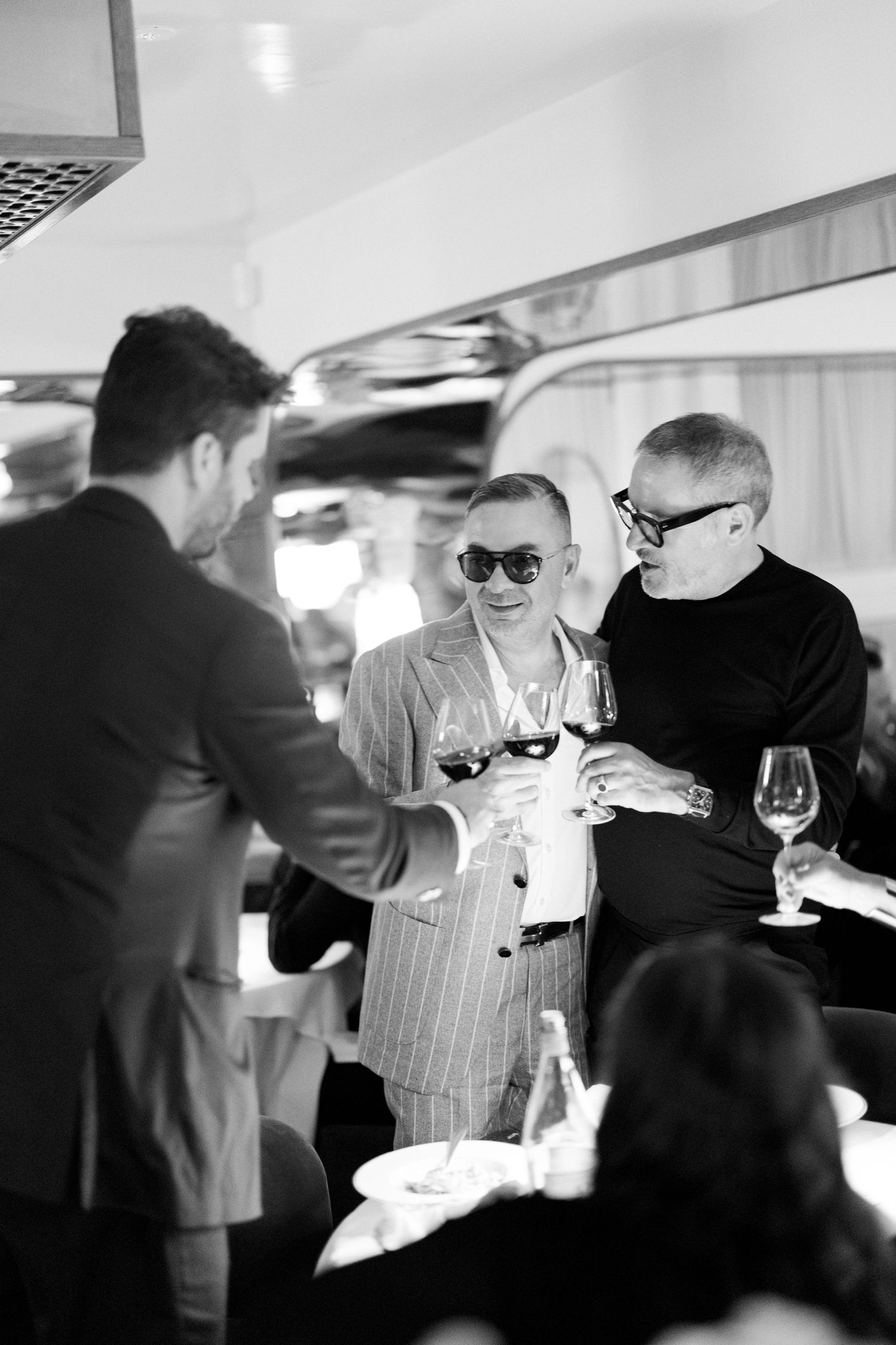 Black and white photo series showing people socializing and holding wine glasses at an elegant gathering.