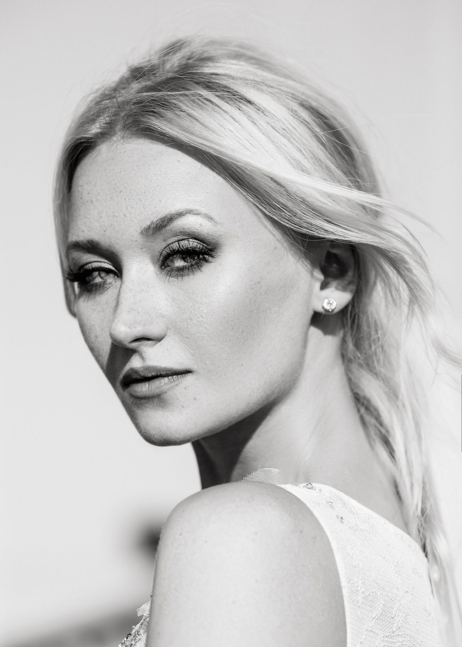 Black and white portrait of a blonde woman with dramatic eye makeup and freckles, wearing a white top.