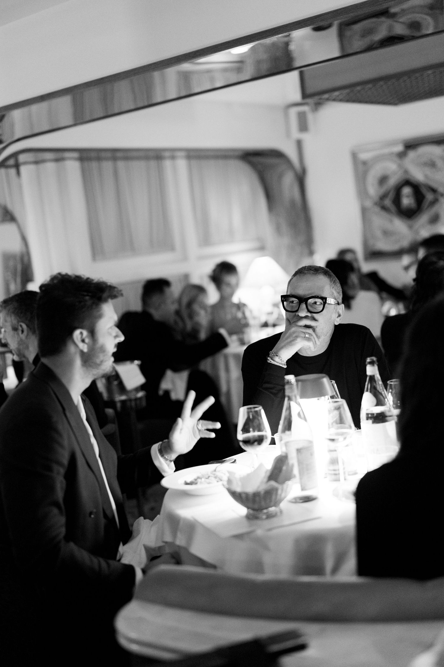 Black and white photo of guests dining at elegantly set tables in a restaurant interior.