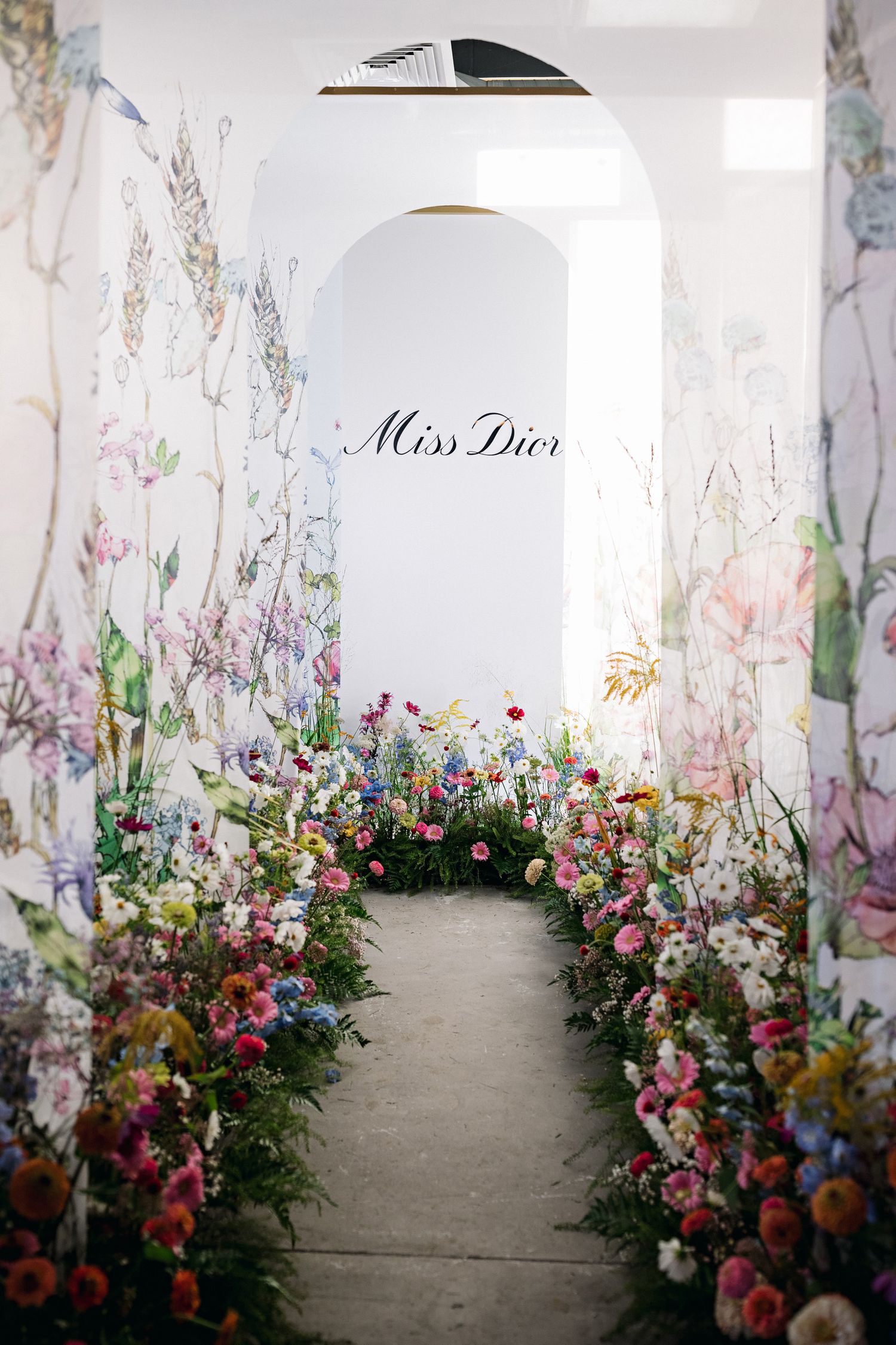 Miss Dior logo archway decorated with colorful wildflowers and garden blooms.