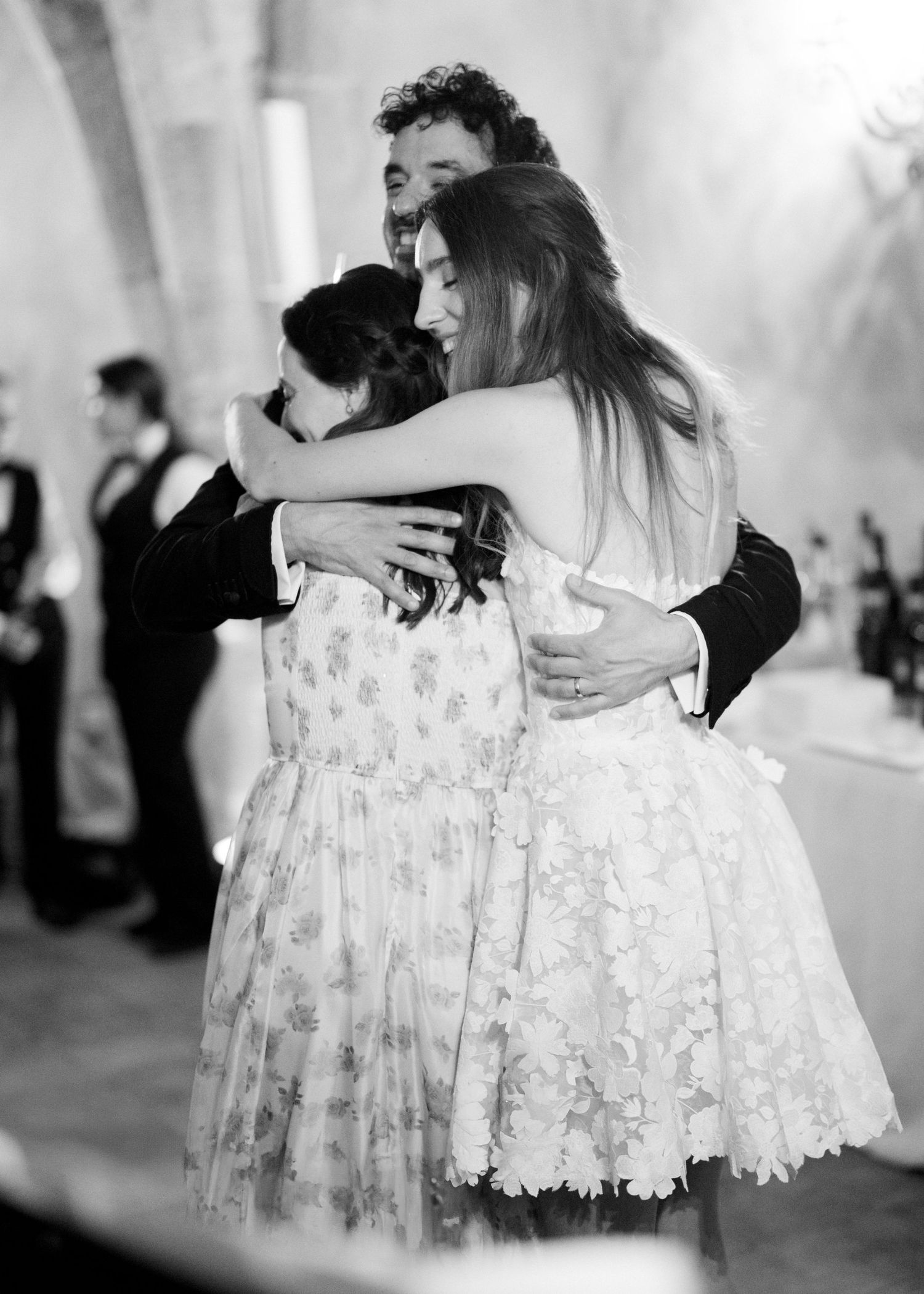 Black and white photo of three people sharing a warm group hug at a formal wedding reception.
