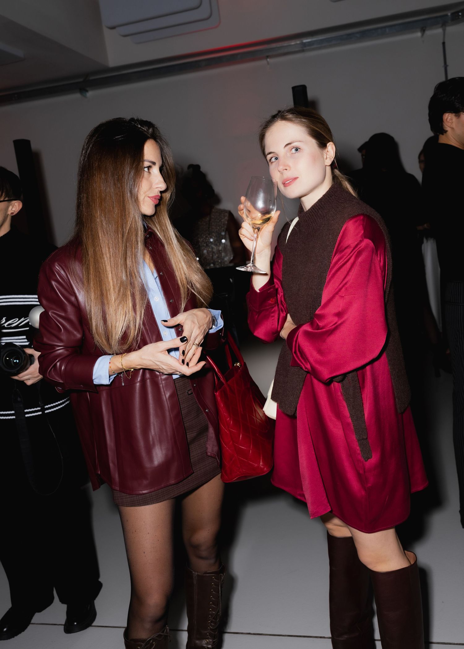 Two people in burgundy outfits socializing at a dimly lit party with drinks.