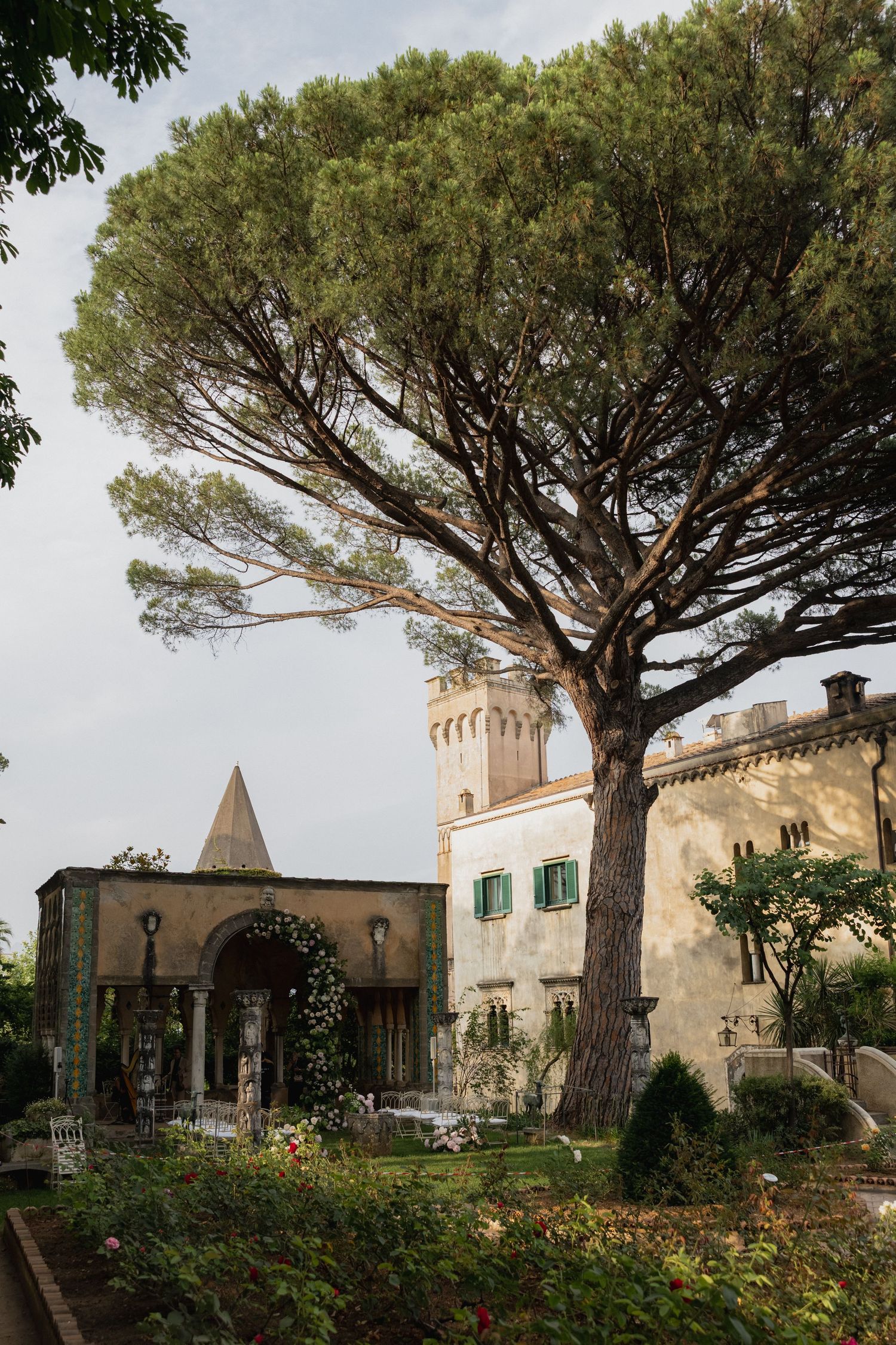 Historic Mediterranean villa with stone walls and umbrella pine trees against a cloudy sky in Ravello, Italy.