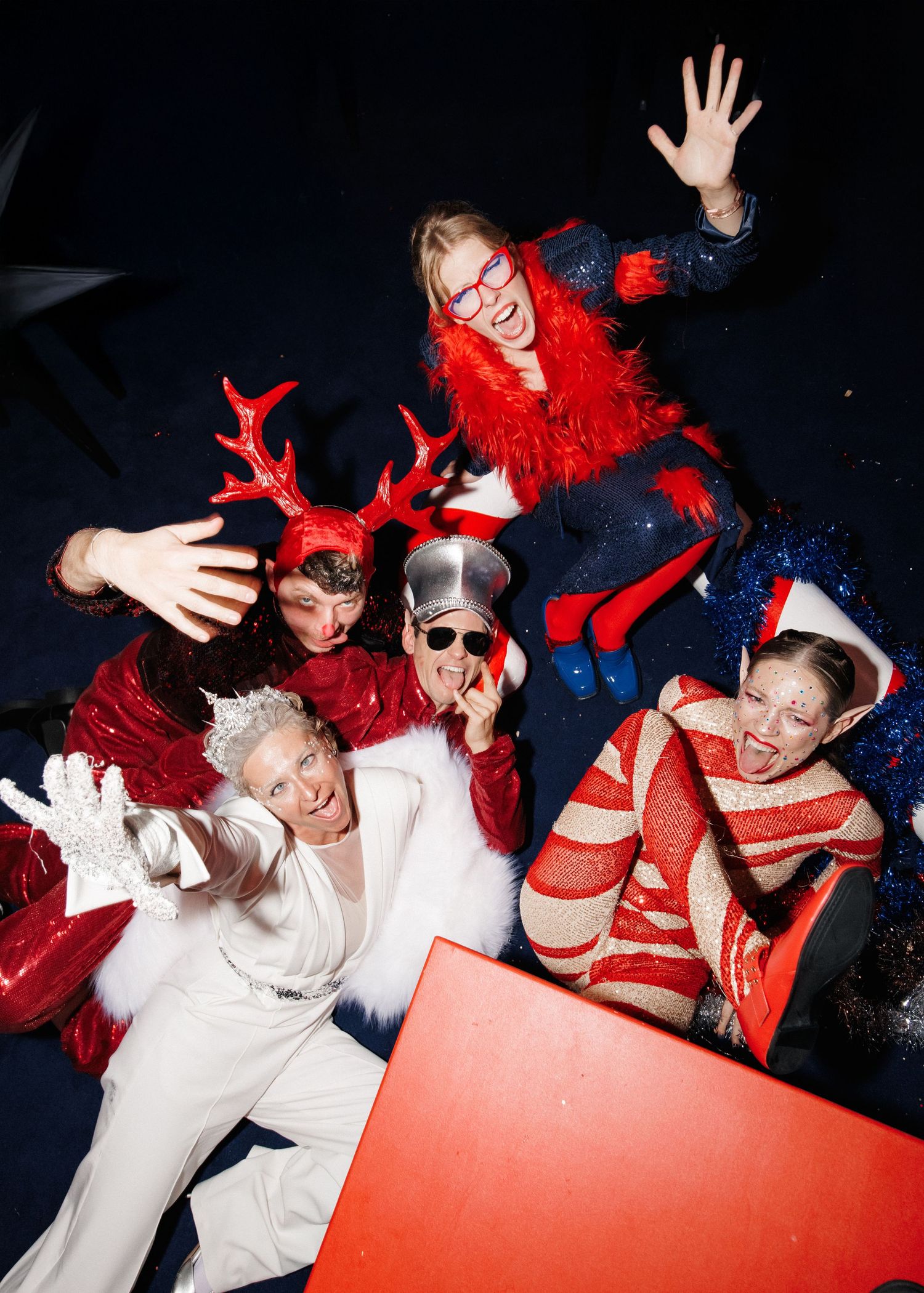 Group wearing festive red and white outfits posing playfully for holiday photo.