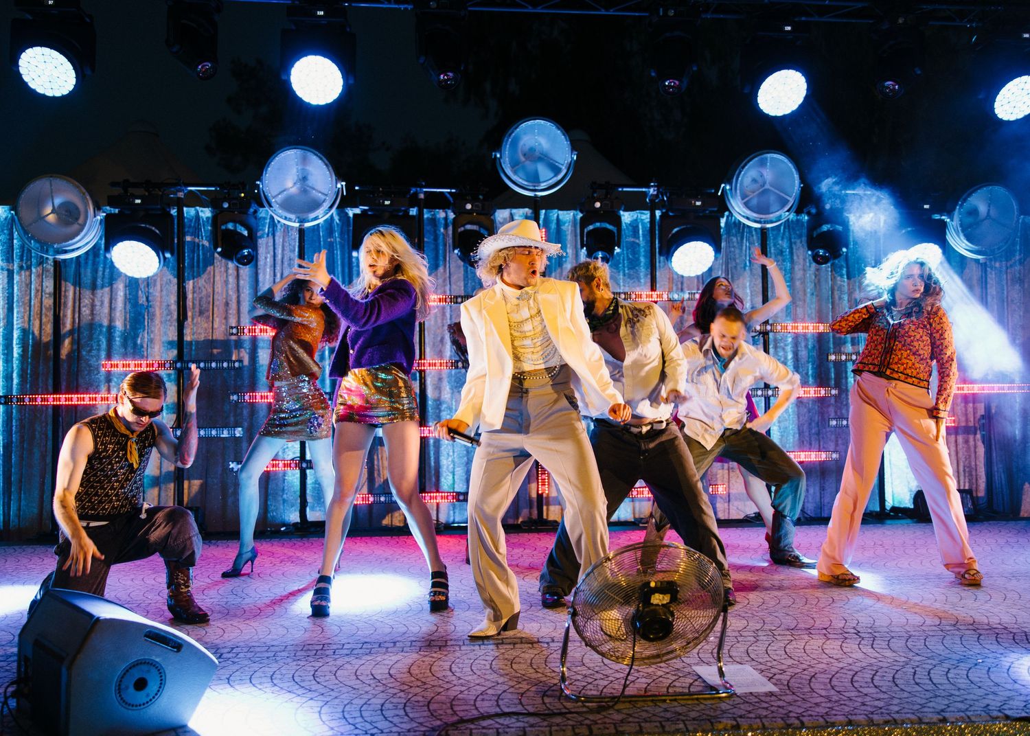 Energetic stage performance with dancers in colorful costumes under blue spotlights.