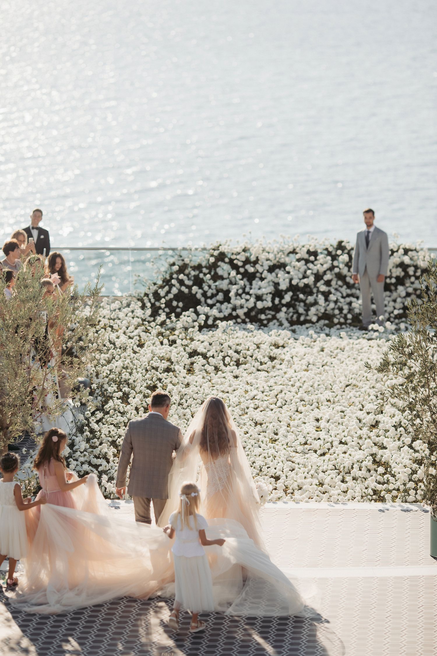 Outdoor wedding ceremony with white floral arch and guests overlooking the ocean.