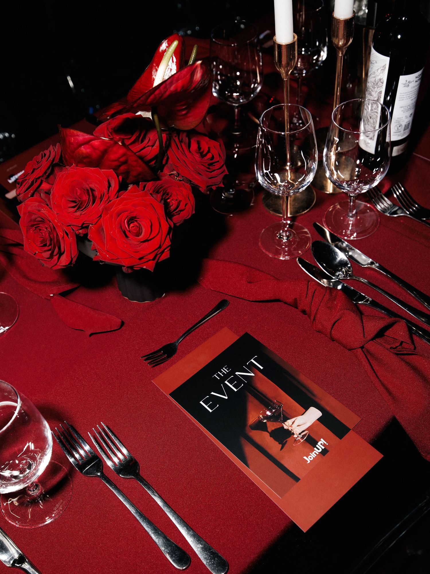 Elegant table setting with red roses, wine glasses and menu on a deep red tablecloth.