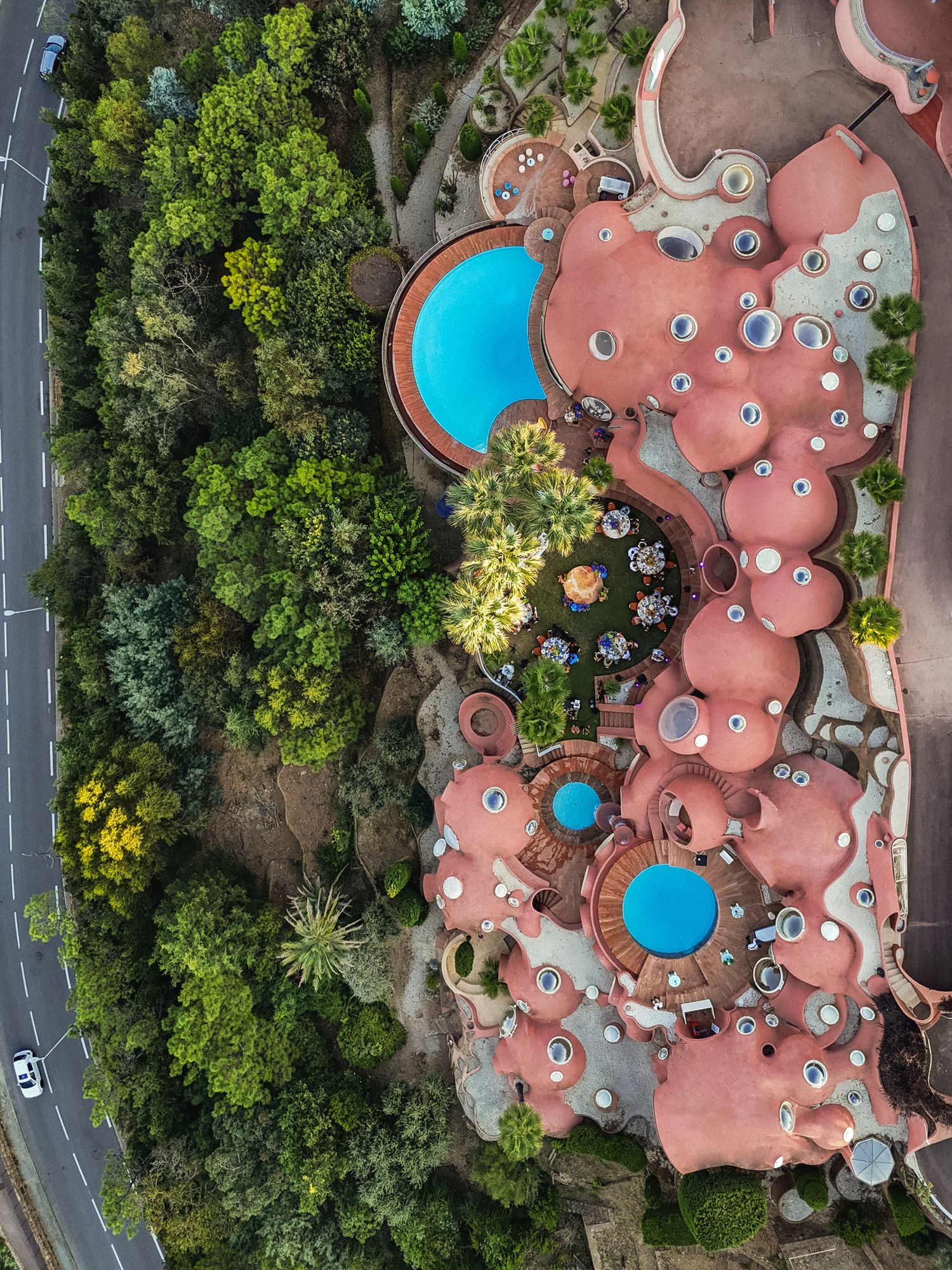 Aerial view of unique bubble-shaped coral-colored architecture with swimming pools and lush landscaping.