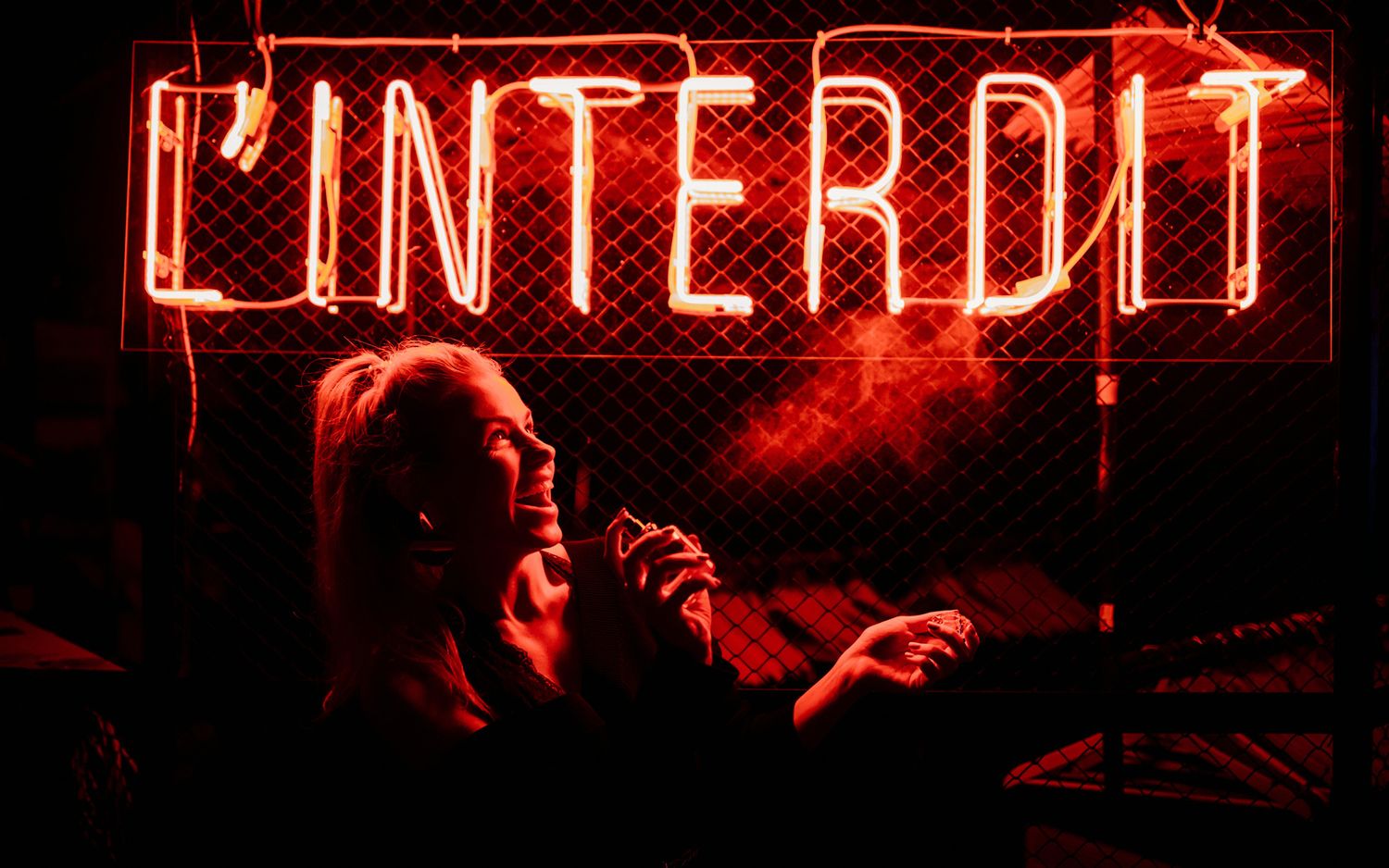 Red neon sign displaying 'L'INTERDIT' in a dark atmospheric setting.
