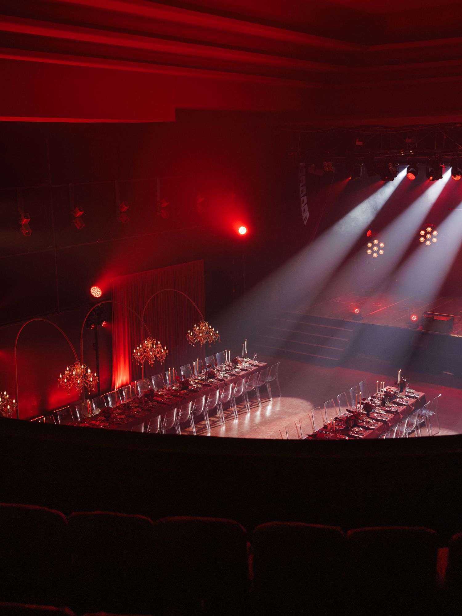 Theater venue with dramatic red lighting and white spotlights illuminating an empty stage setup.