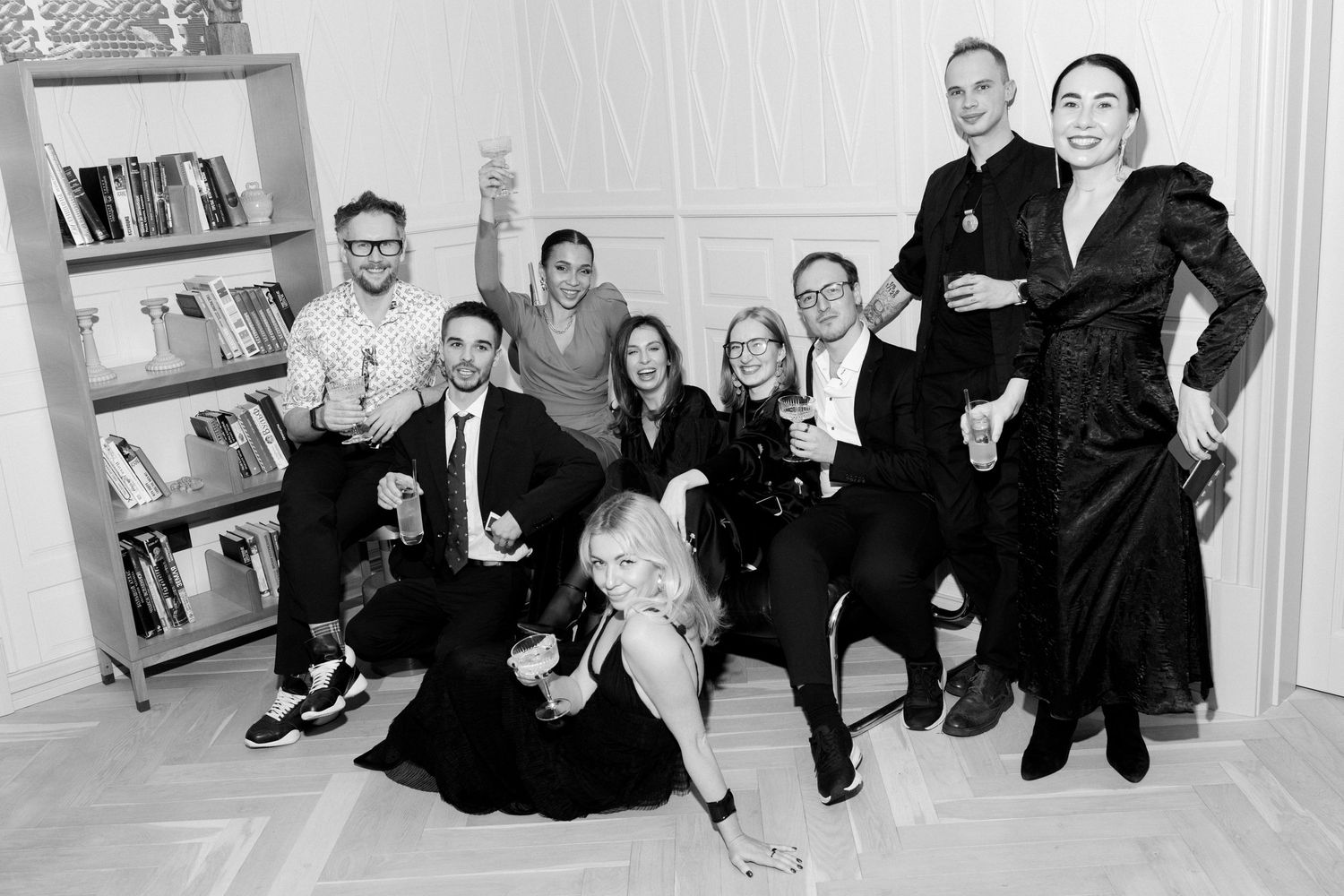 Group photo in black and white with people sitting and standing against a white wall with bookshelves.