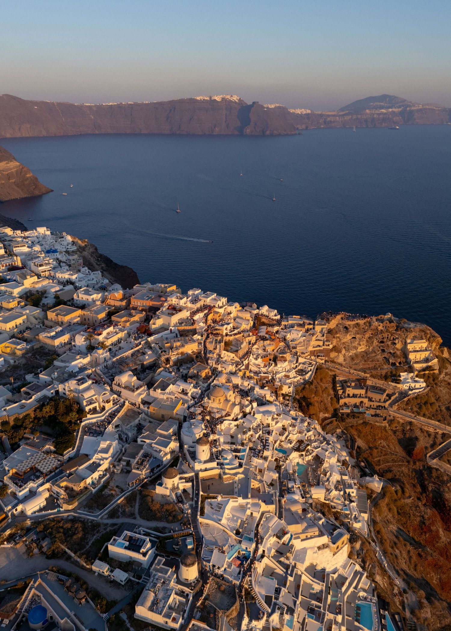 Aerial view of white buildings cascading down Santorini's cliffs overlooking the Mediterranean Sea.