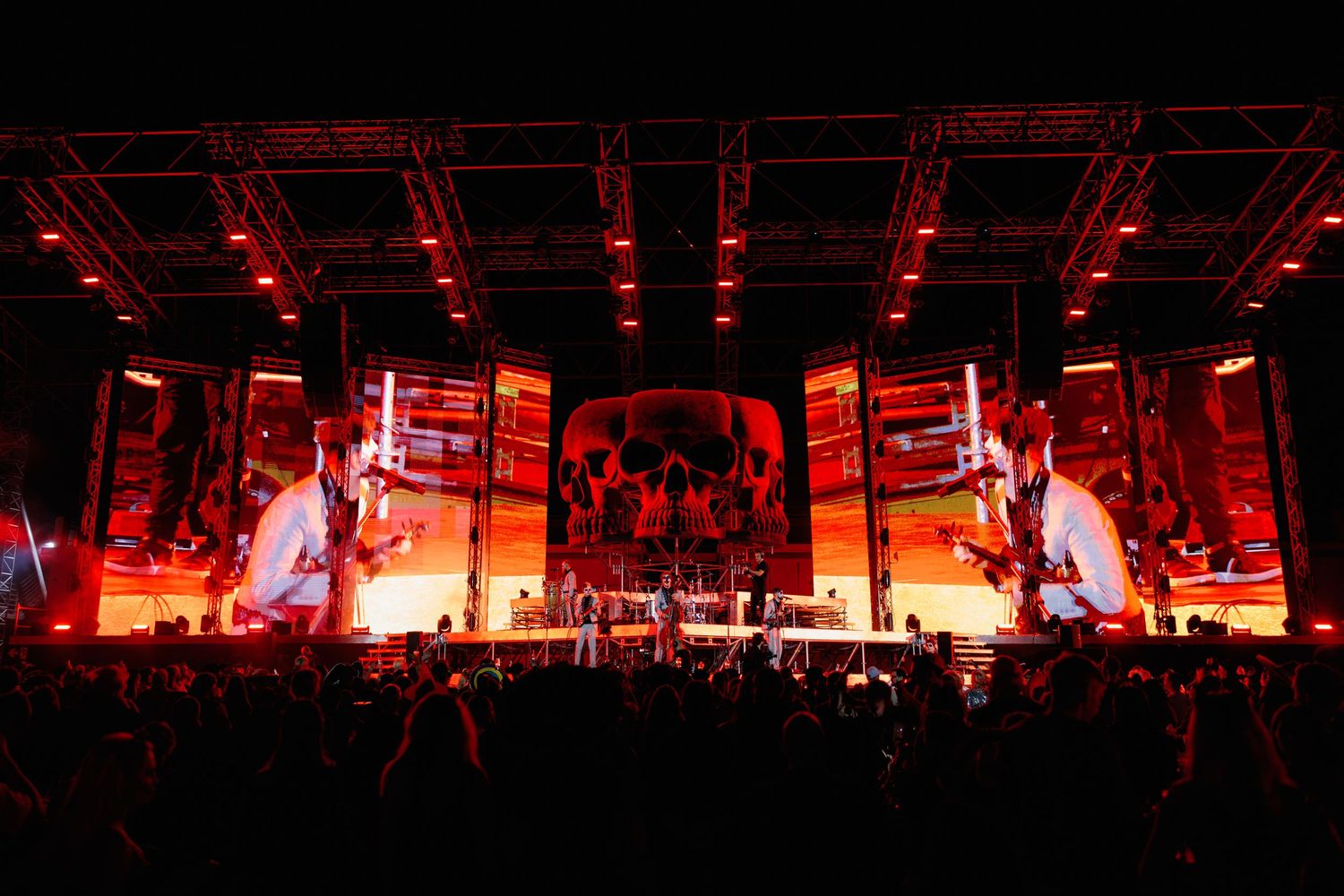Large concert stage with massive LED screens displaying red visuals during performance.