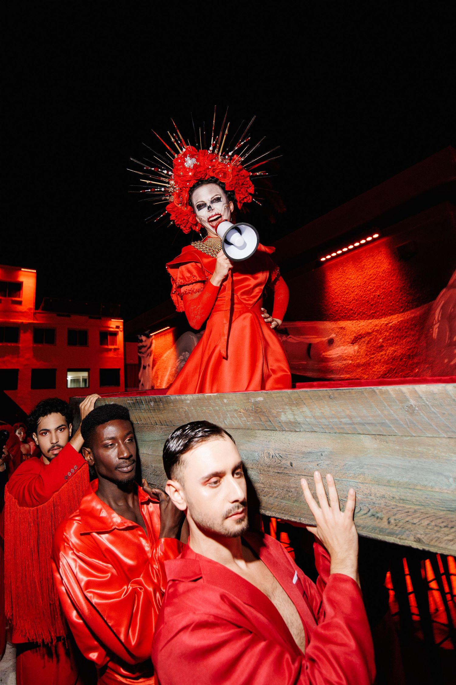 Dramatic fashion scene with performers in red costumes against dark background.