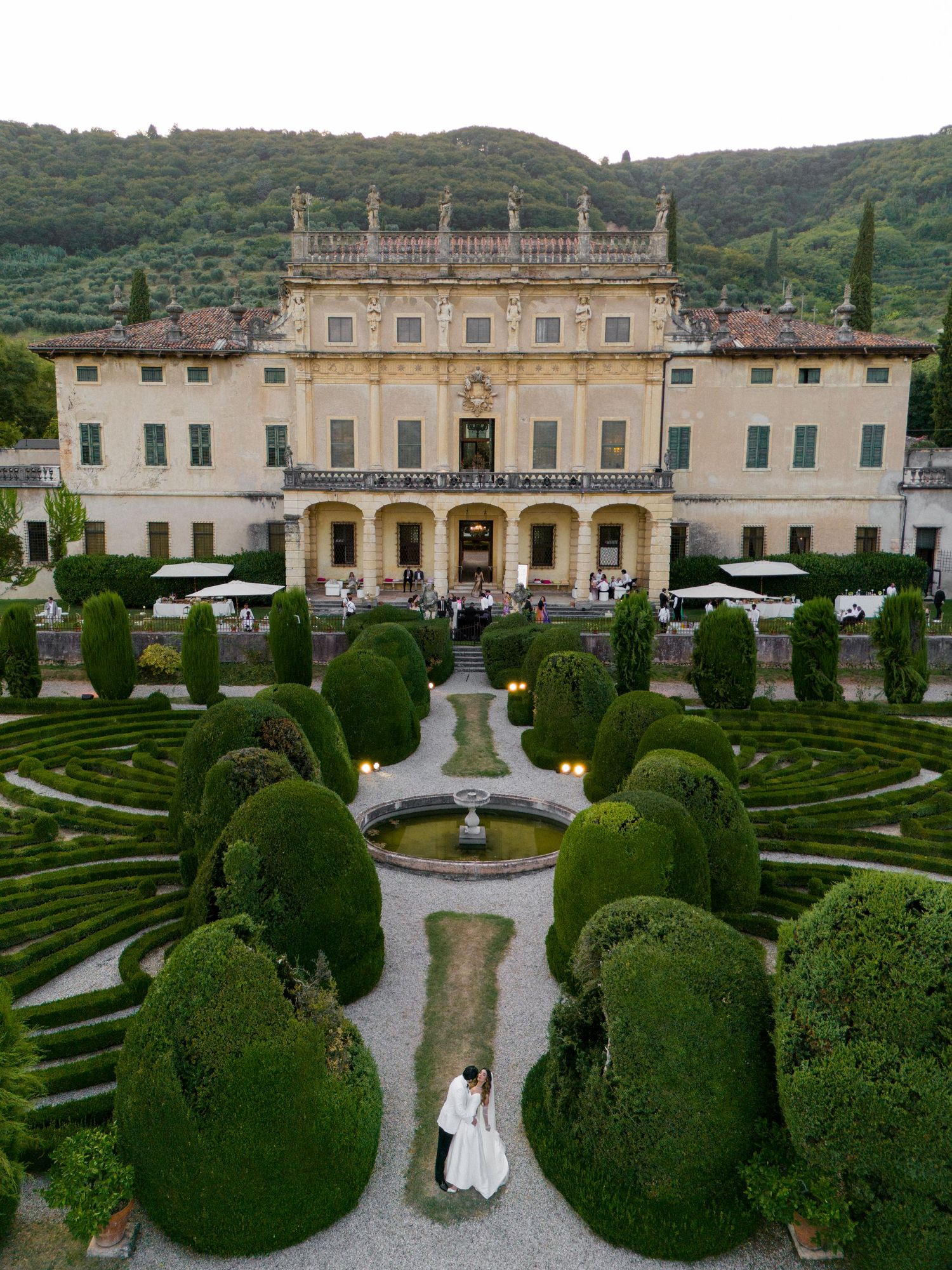 Aerial view of grand Italian villa with manicured hedge gardens and ornate fountain.