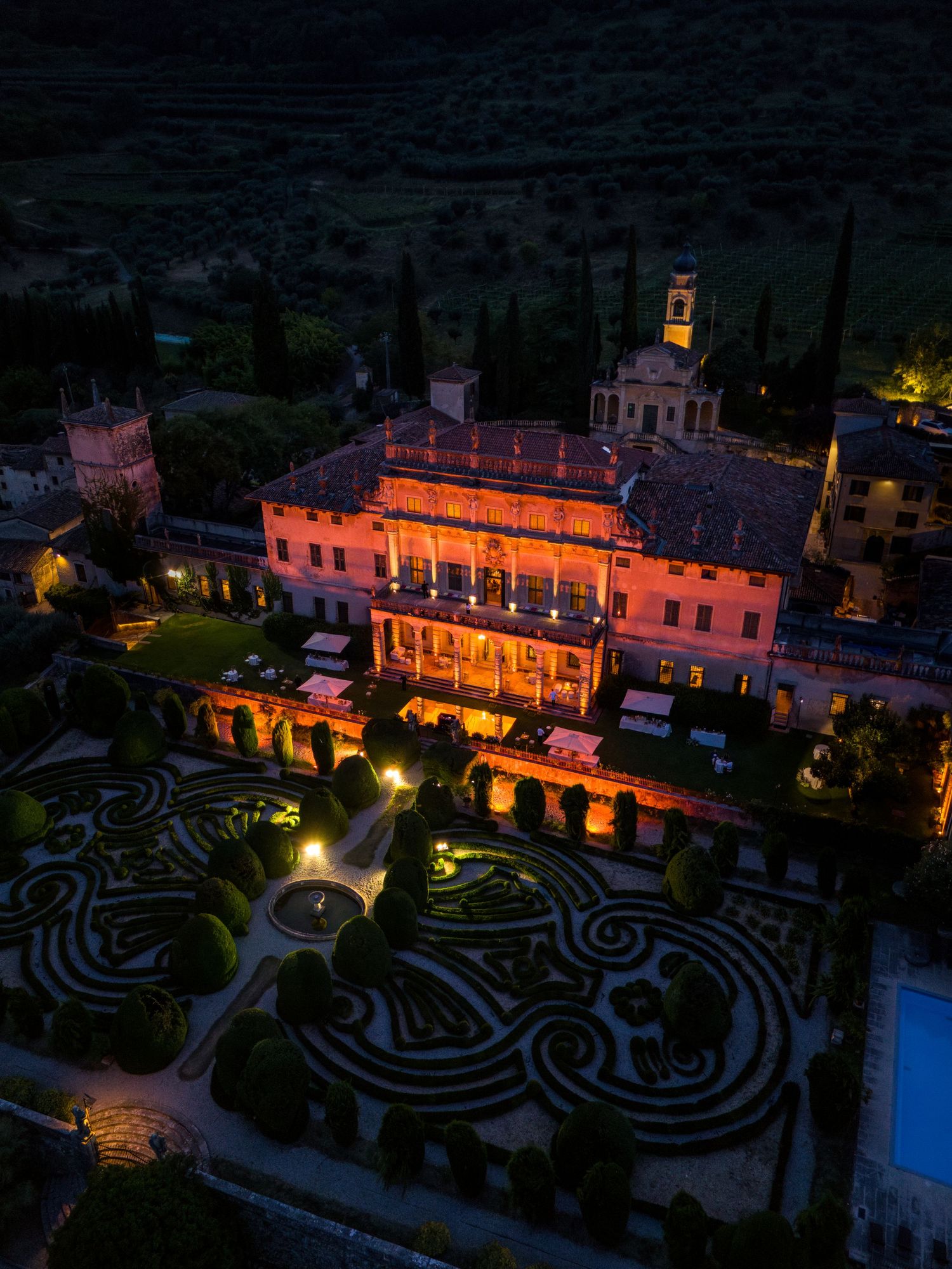Illuminated villa with ornate gardens and maze-like patterns photographed at dusk in Italy.
