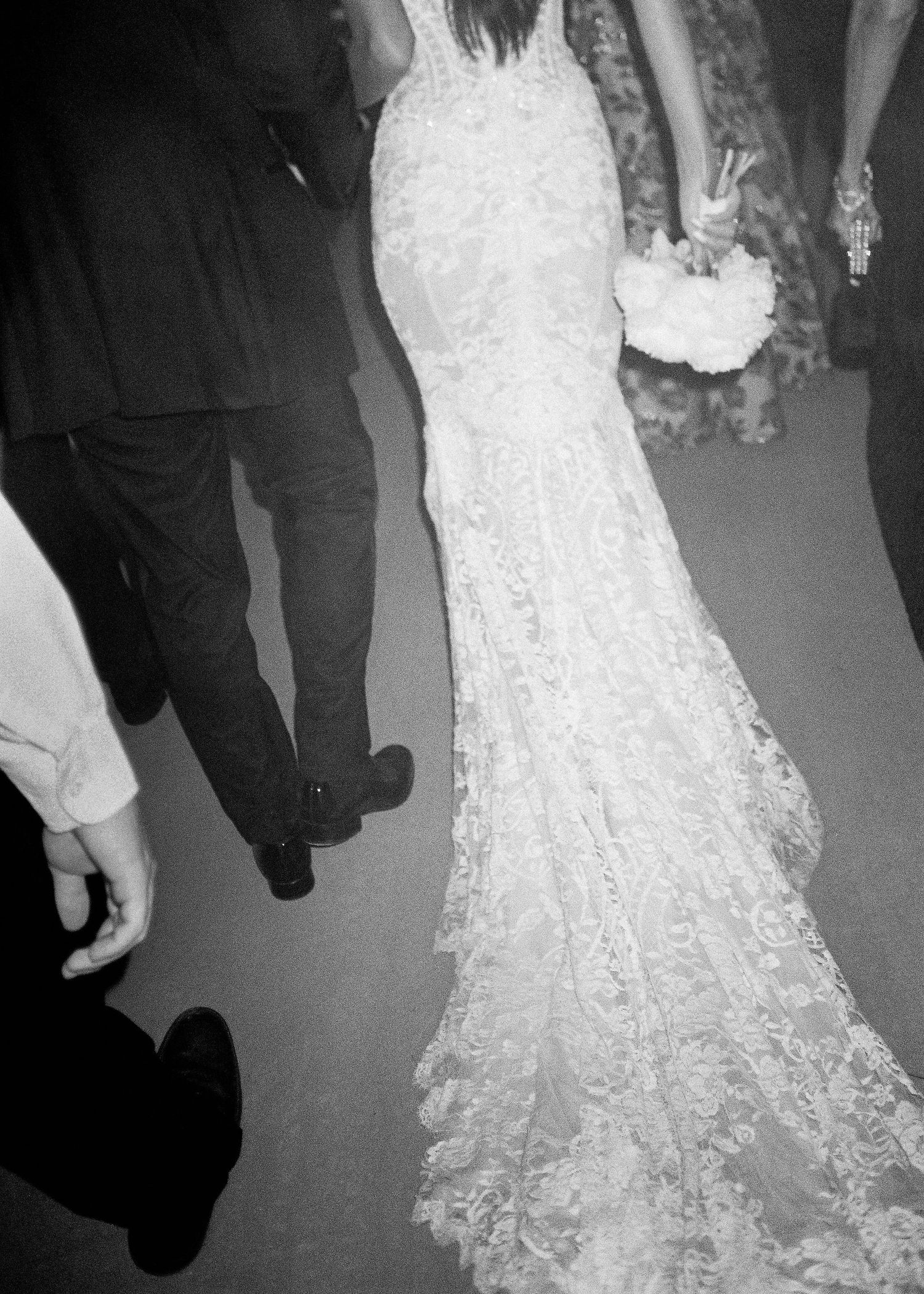 Black and white photo of a bride in an elegant lace mermaid wedding gown with a train, holding a white bouquet.