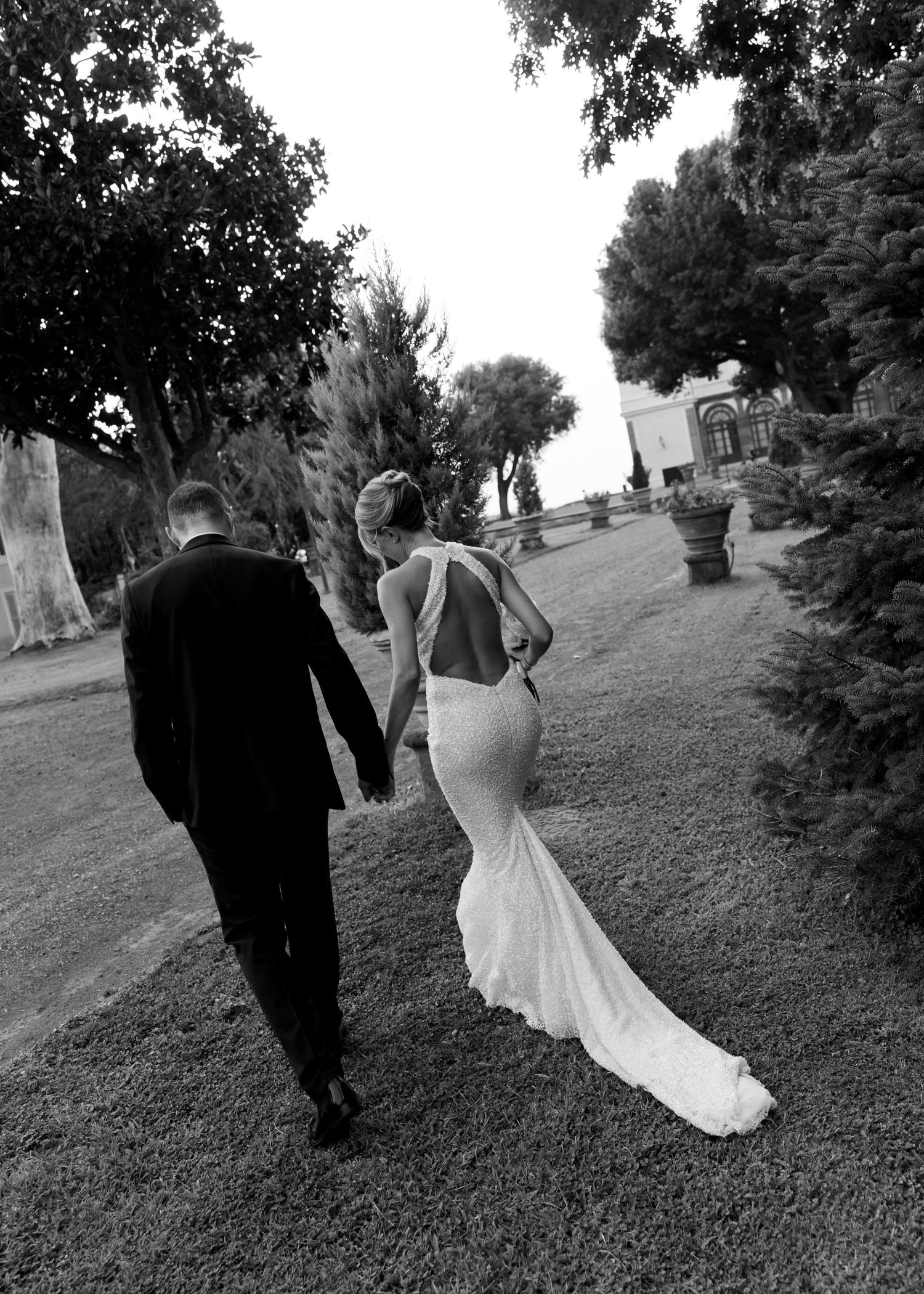 Black and white photo series shows a couple walking up a grassy hillside in formal wedding attire.