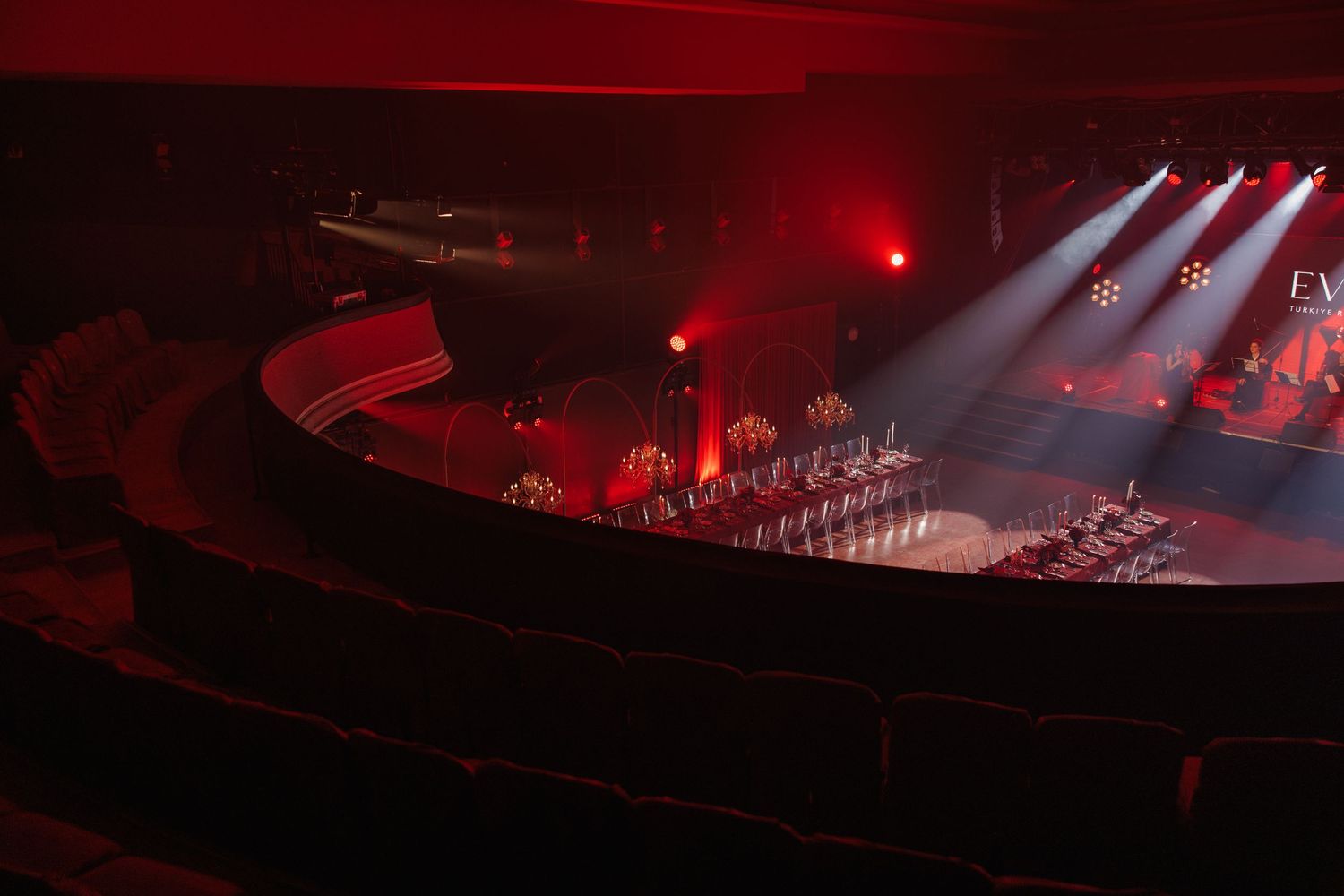 Concert venue with dramatic red lighting and fog effects illuminating the stage.