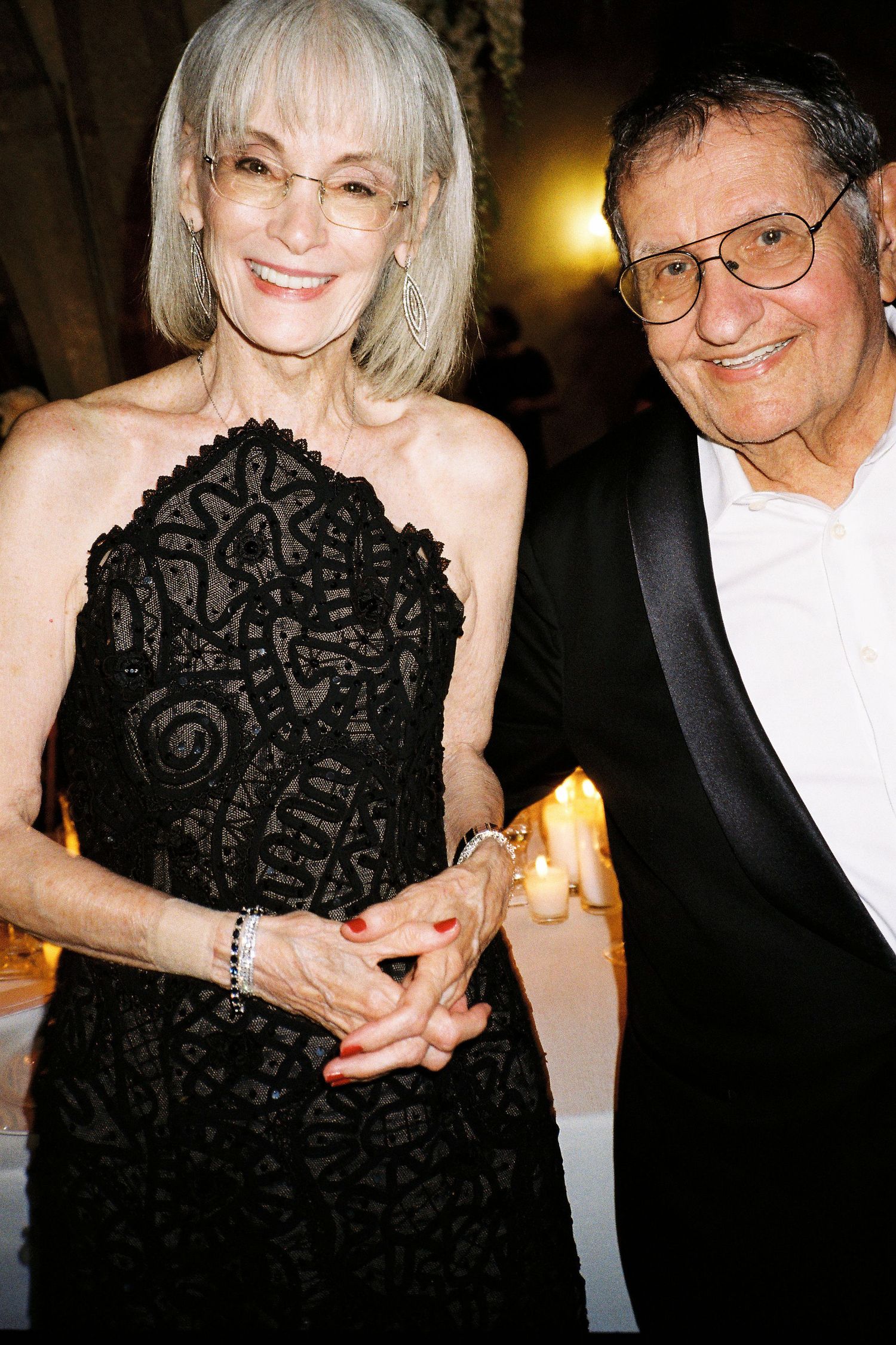 A person wearing a black lace dress poses with a warm smile at an elegant evening event.