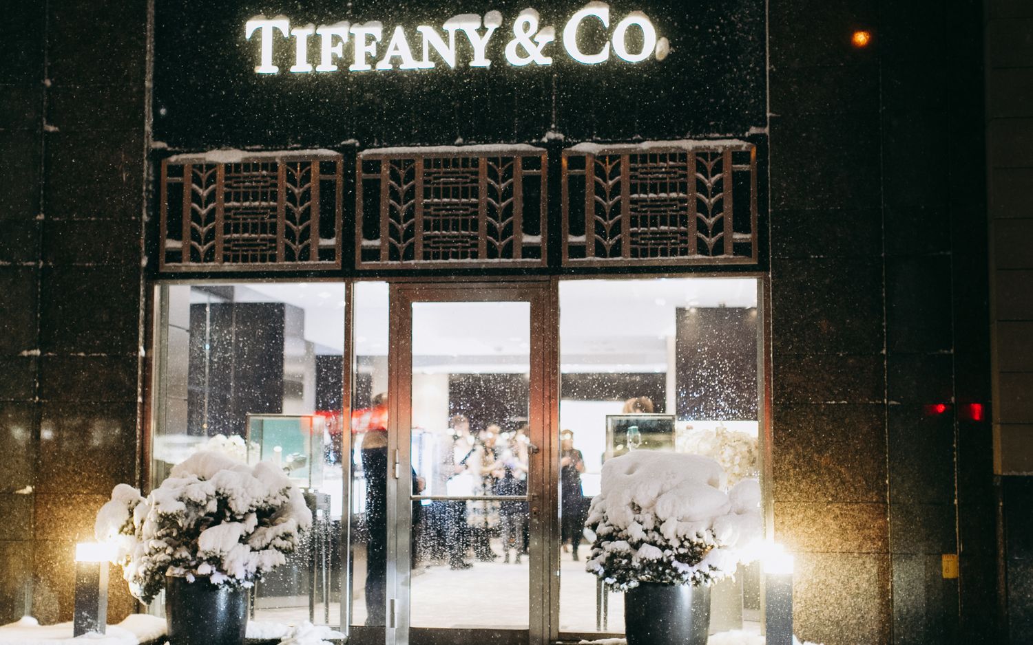 Illuminated Tiffany & Co storefront with holiday decorations and floral arrangements.