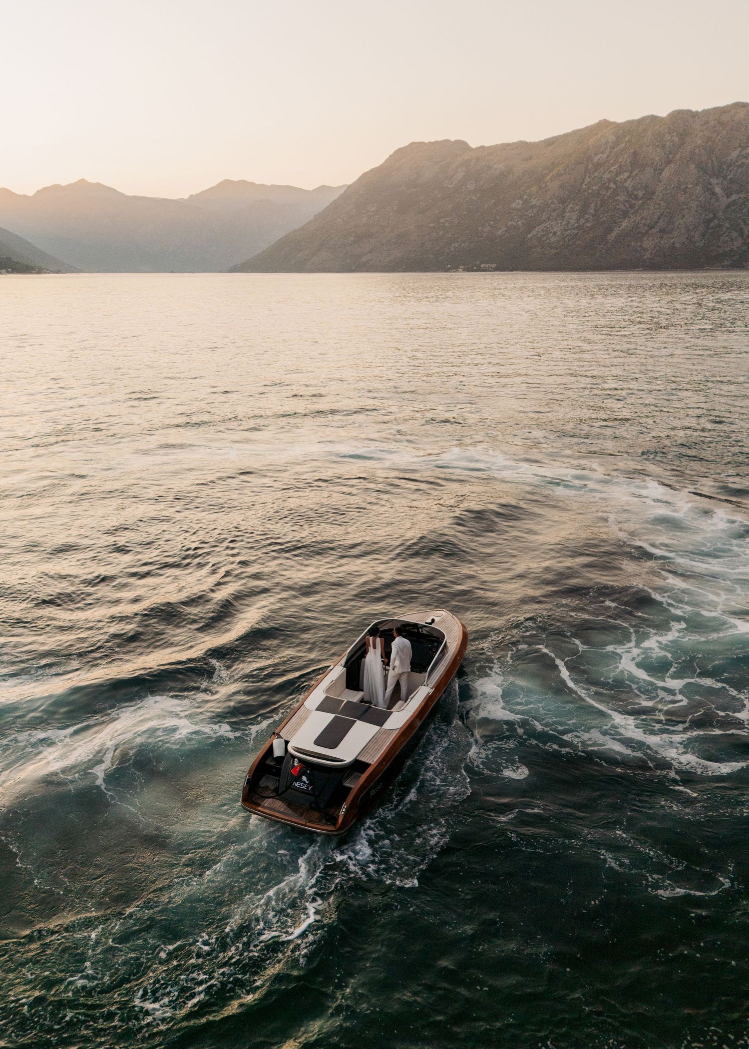 Aerial view of a classic wooden speedboat cruising on a serene mountain lake at golden hour.