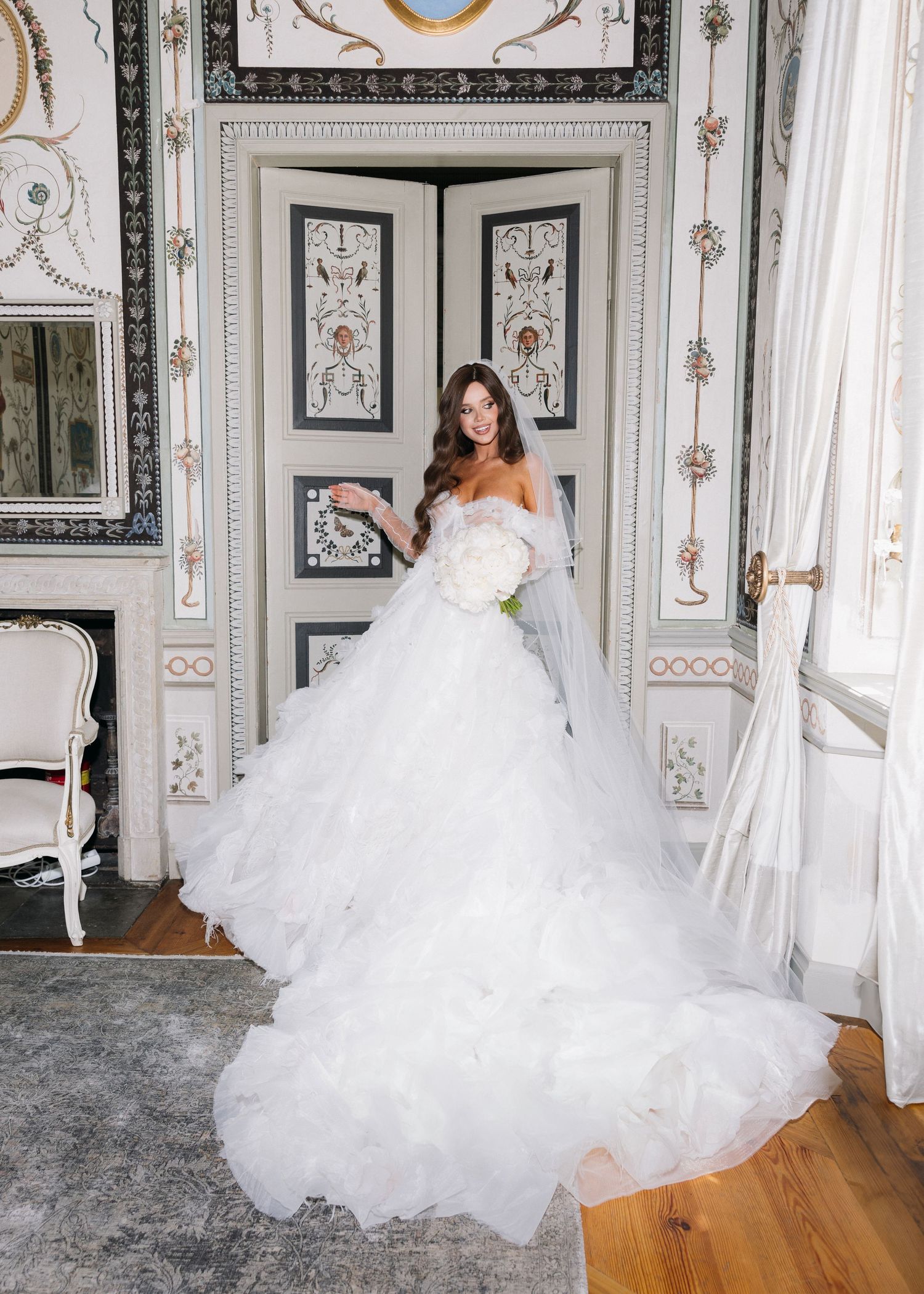 Elegant bride in strapless white ballgown with dramatic tulle train poses in front of ornate vintage doorway.
