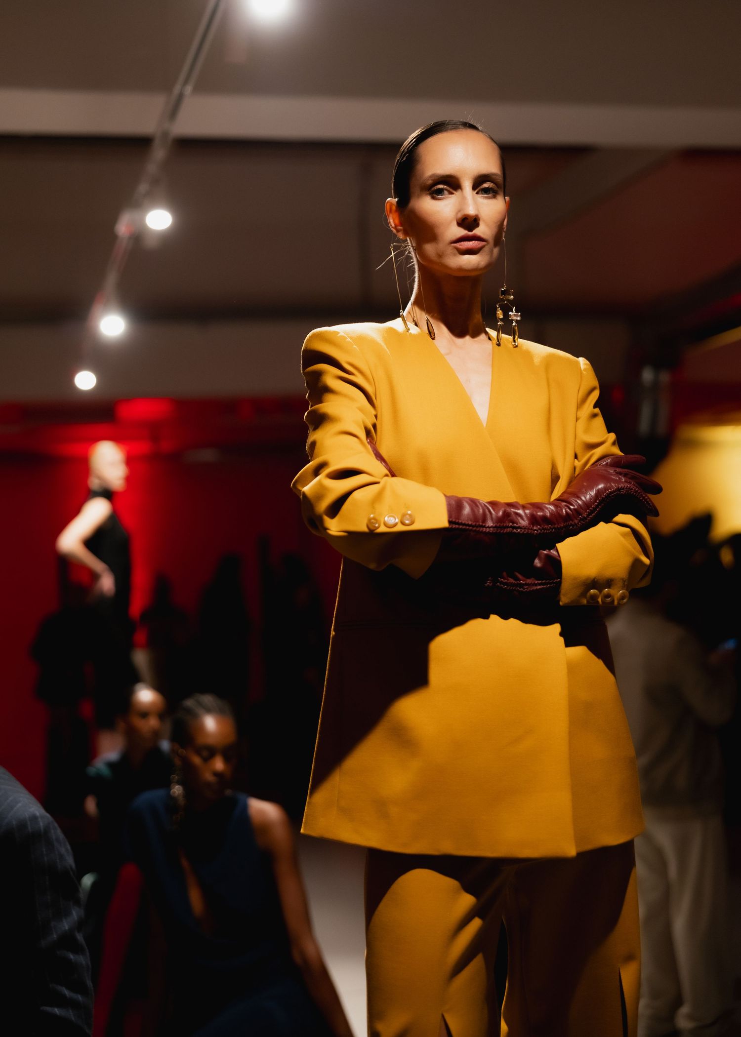 A model showcases a vibrant yellow power suit in a dimly lit fashion event setting.