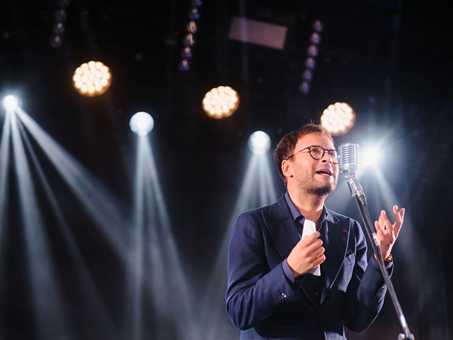 A performer on stage illuminated by dramatic spotlights during a show.