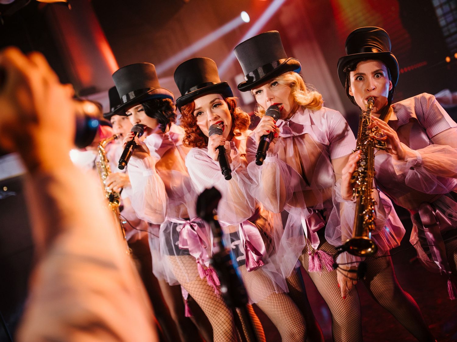 Performers in white outfits and top hats dance on stage during a cabaret-style show.