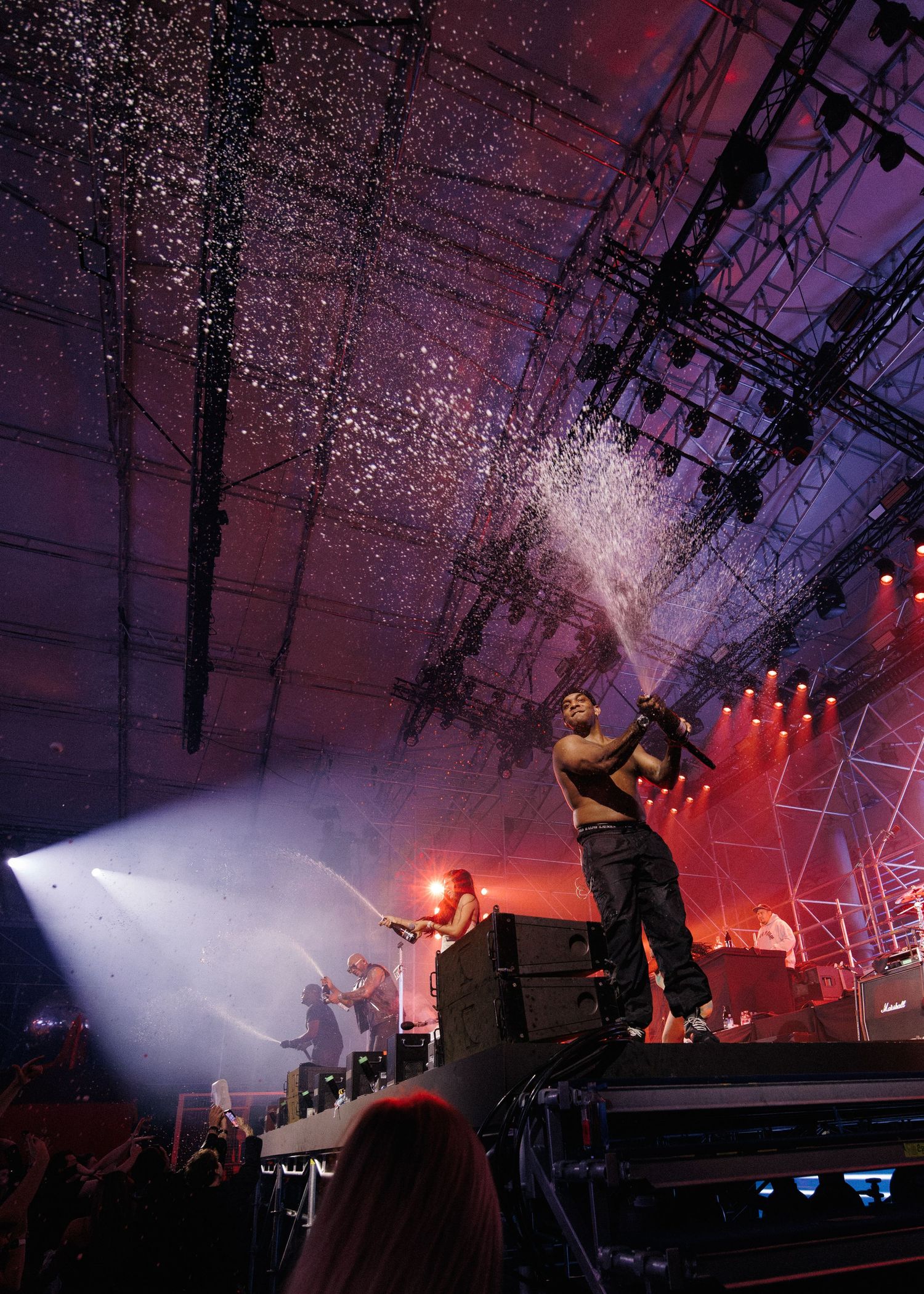 Concert performer spraying water into crowd during dramatic light show on stage.
