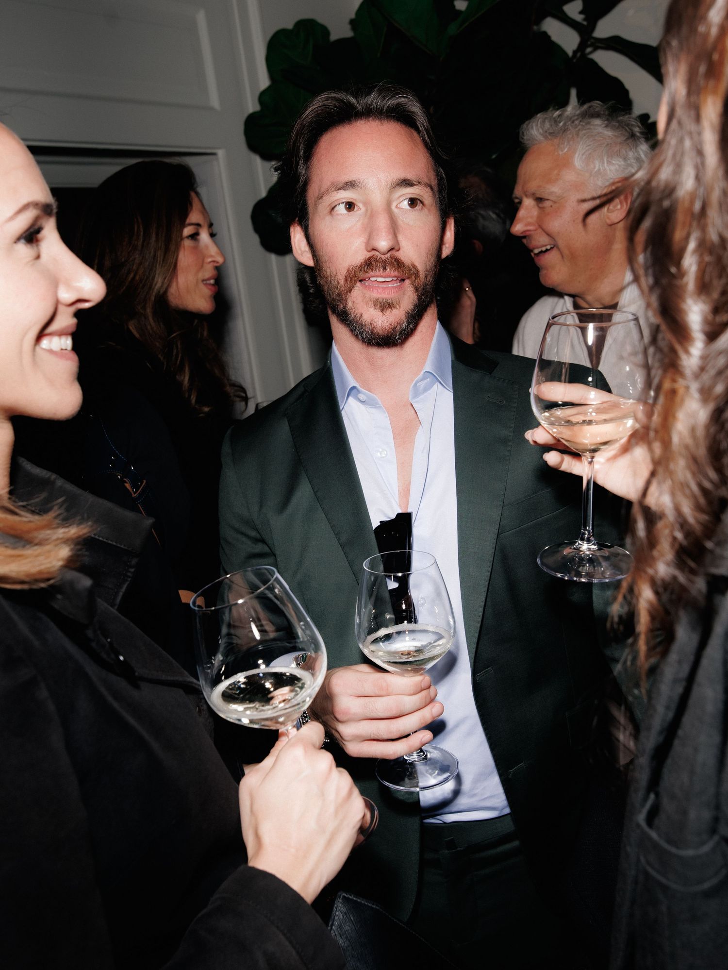 People socializing and holding wine glasses at an indoor gathering with dark lighting and casual ambiance.