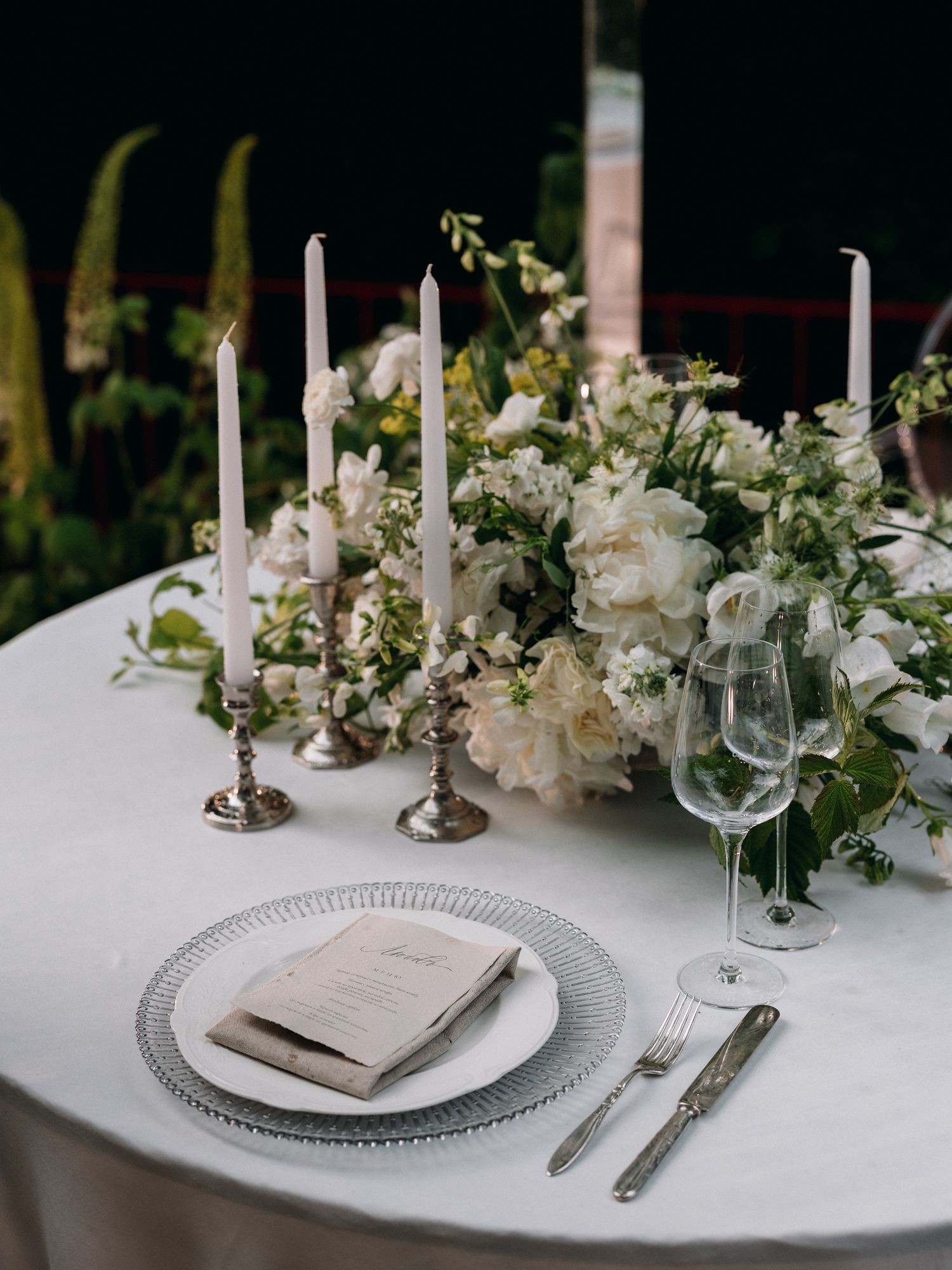 Elegant table setting with white candles and floral centerpiece at formal dinner.