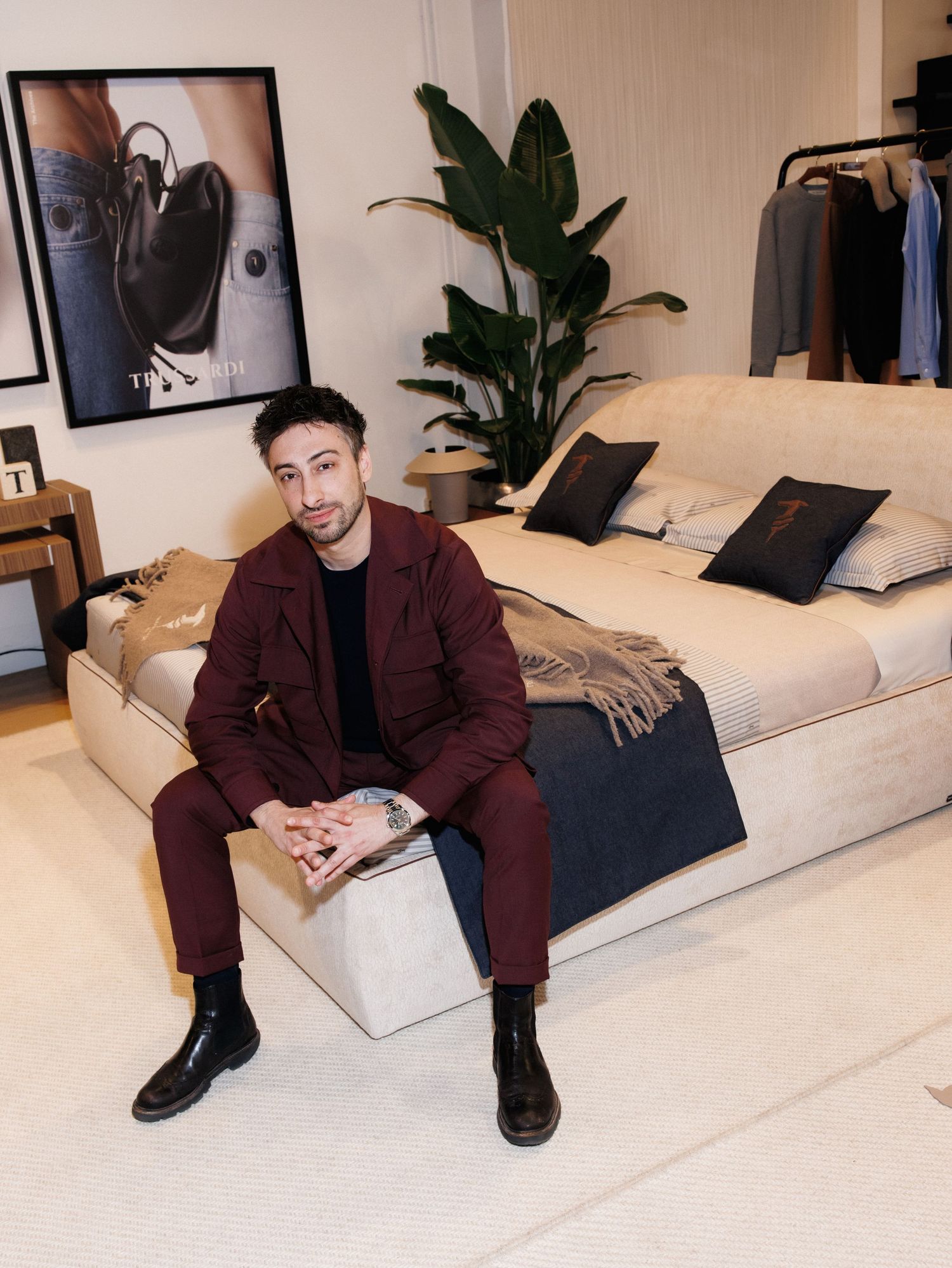 Person in burgundy suit sits on white modern sofa in contemporary room with potted plant decor.