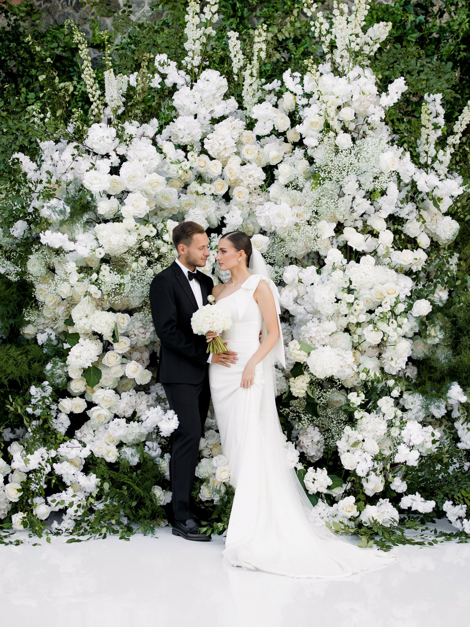 Elegant wedding portrait against lush white floral wall installation.